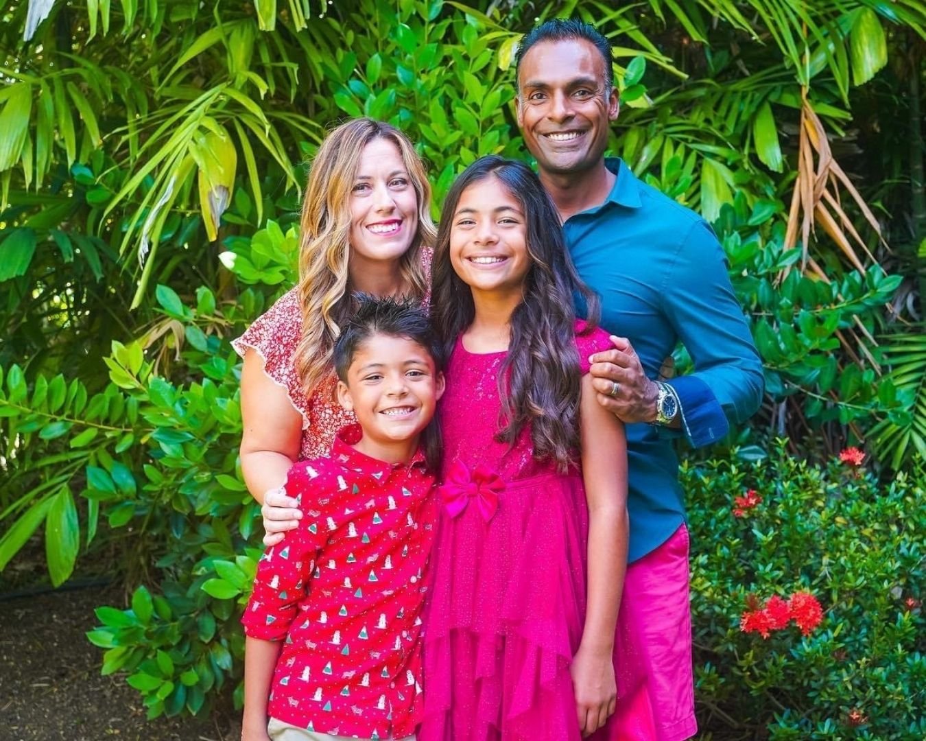 Family of four: mom, dad, son, and daughter standing in front of green tropical plants.