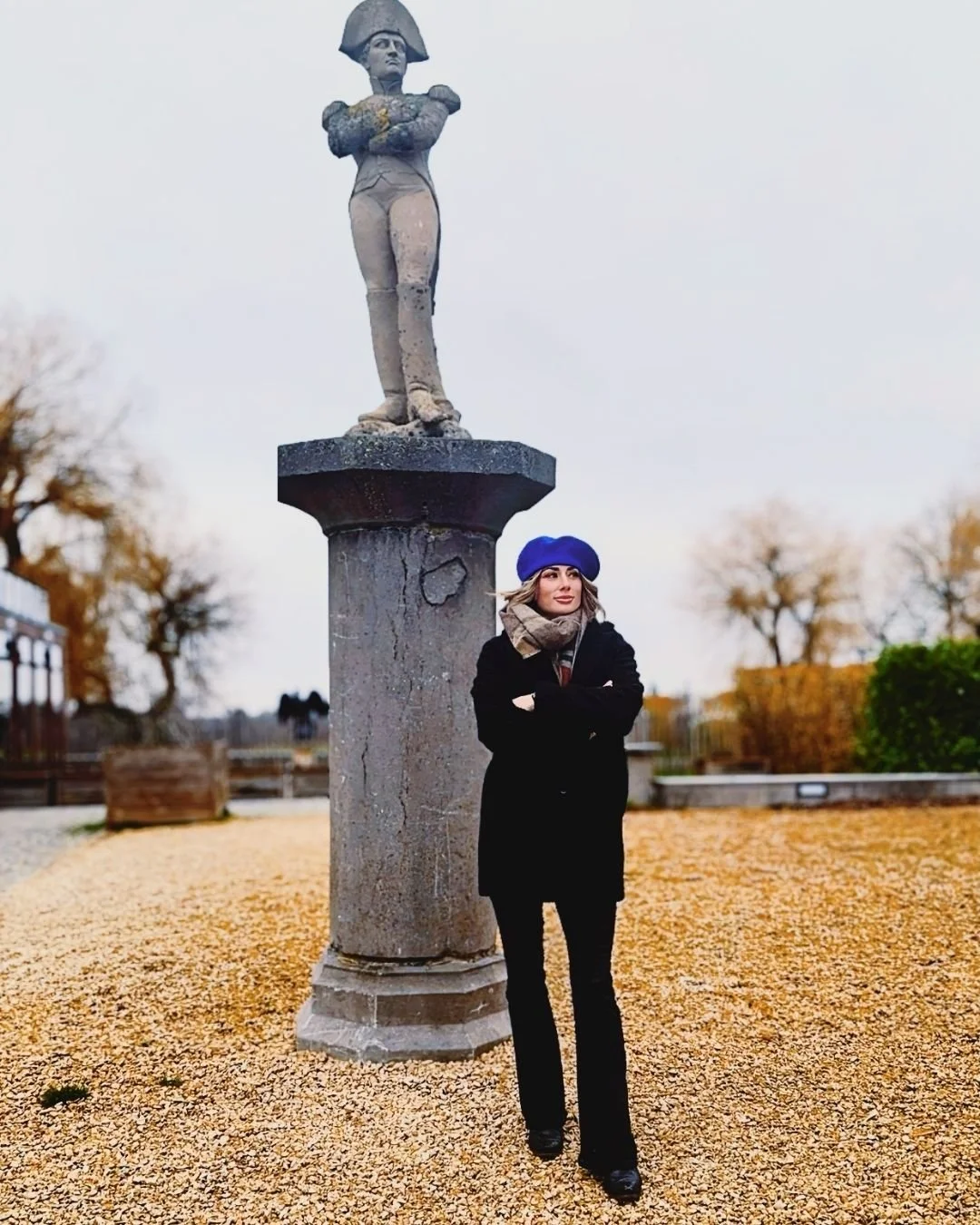 Woman in black clothes and blue beret in front of statue of Napolean