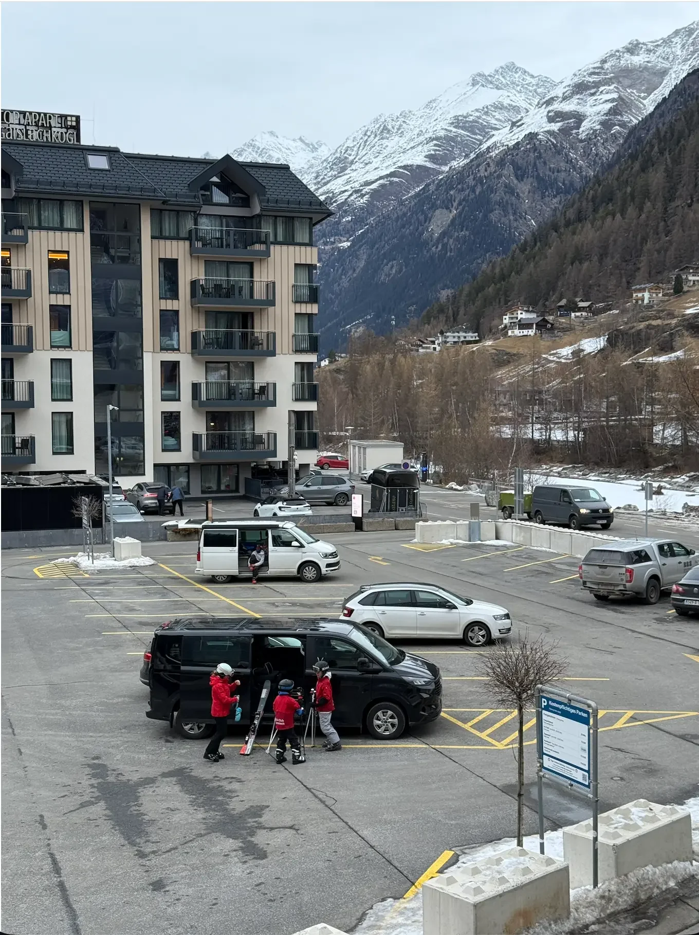 Van in a mountain parking lot with 3 kids getting their skis out.