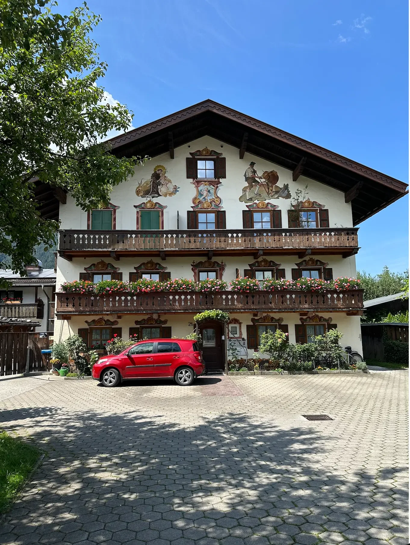 Small red car parked in front of Bavarian house with traditional frescoes and flower boxes.