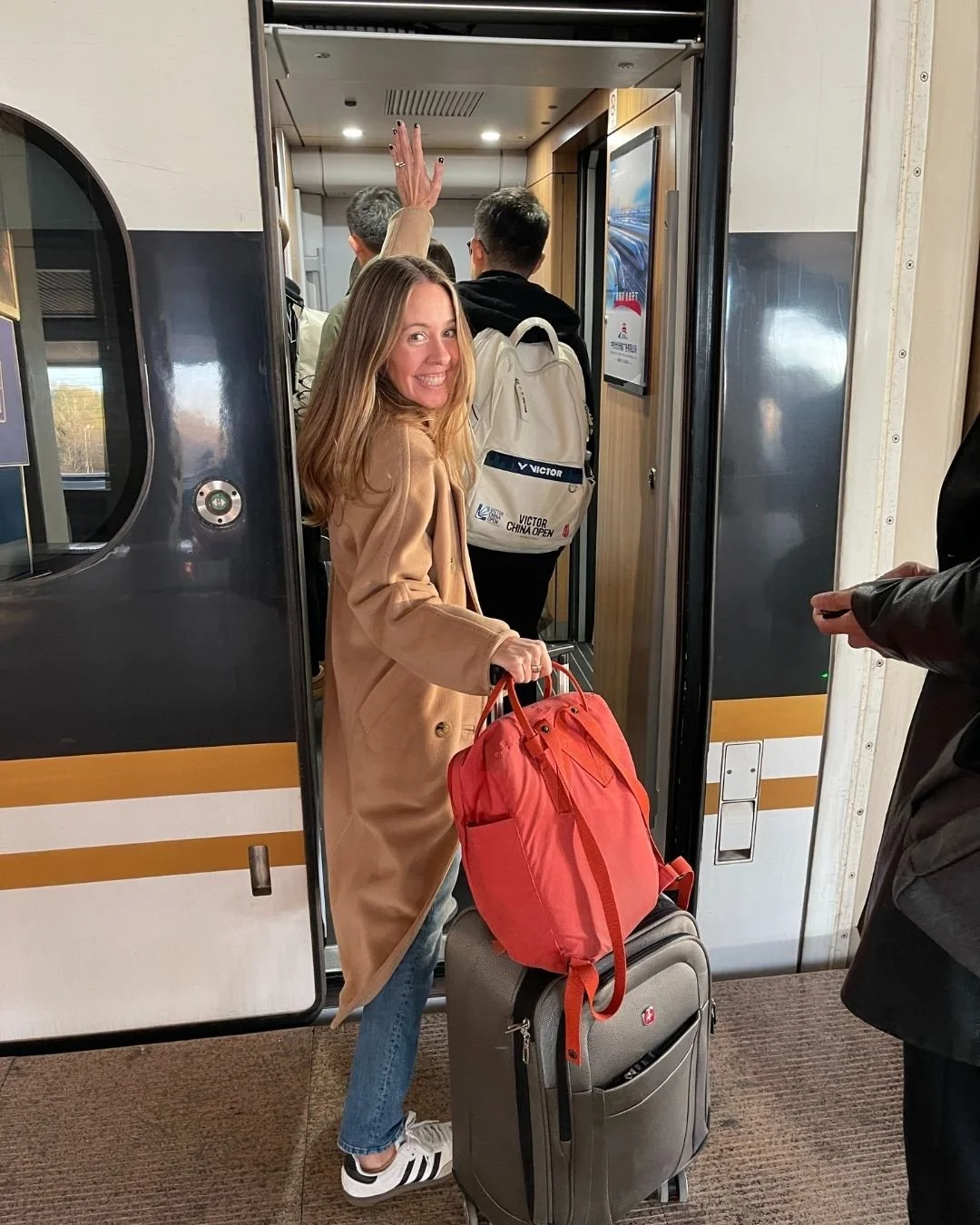 Woman boarding a train in China with her luggage looking back to the camera and smiling.