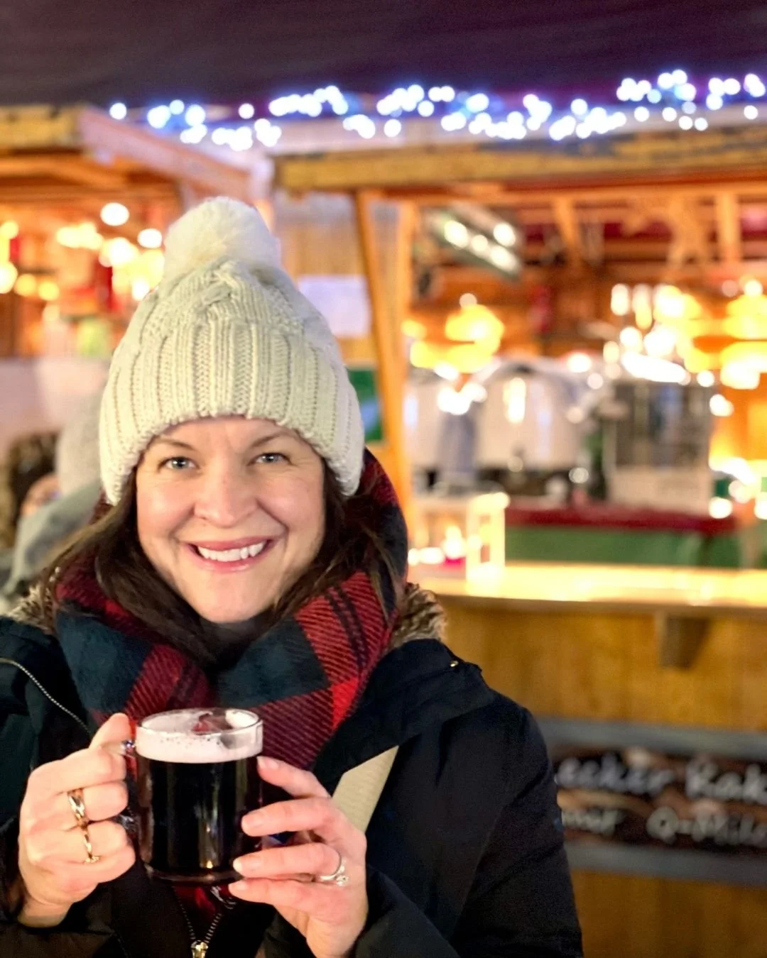 Woman in winter clothes holding a mug of gluhwein with Christmas market stalls in the background