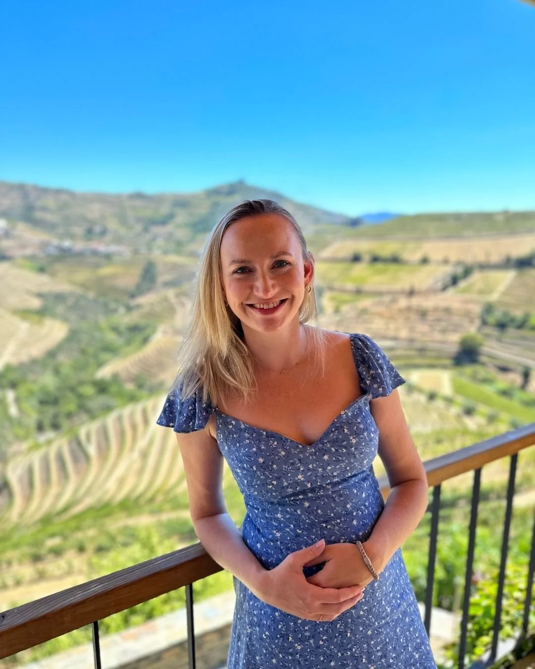 Woman on a balcony with rolling hills in the background.