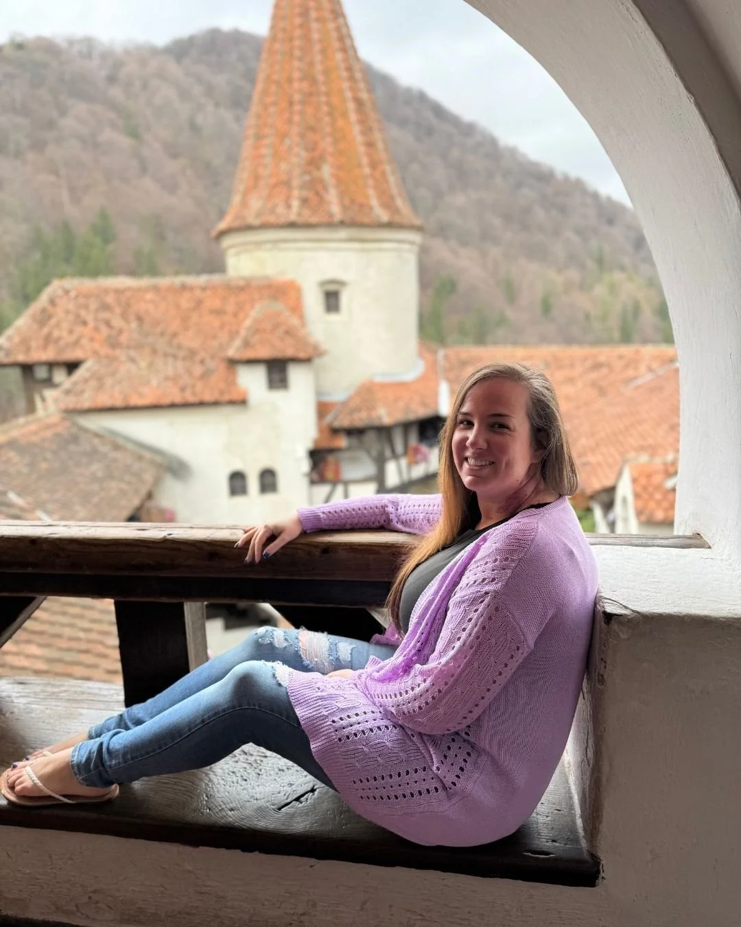 Woman sitting on a windowsill of a castle with castle turets and building in the background