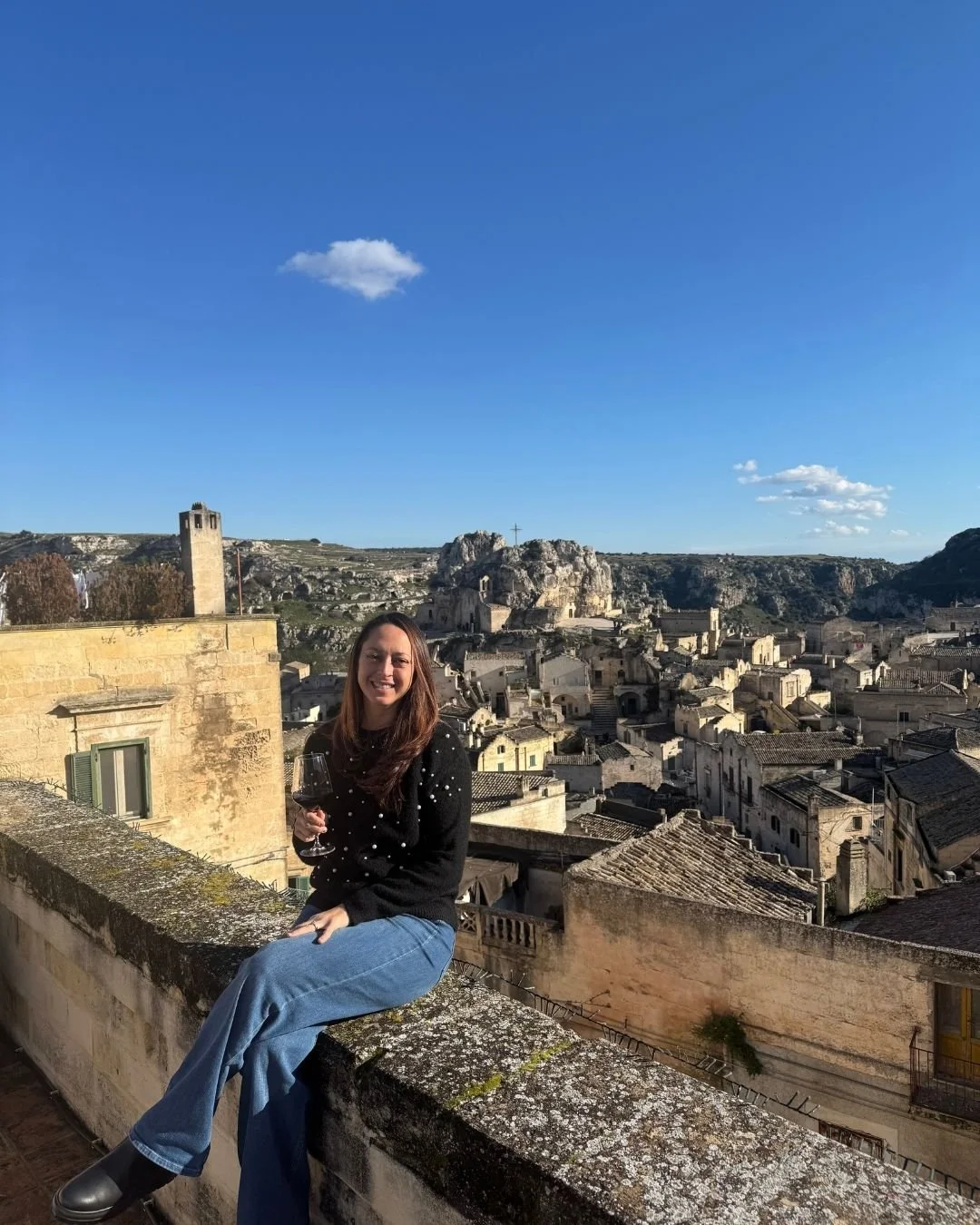 Woman sitting on the edge of a balcony with a glass of wine in an Italian village