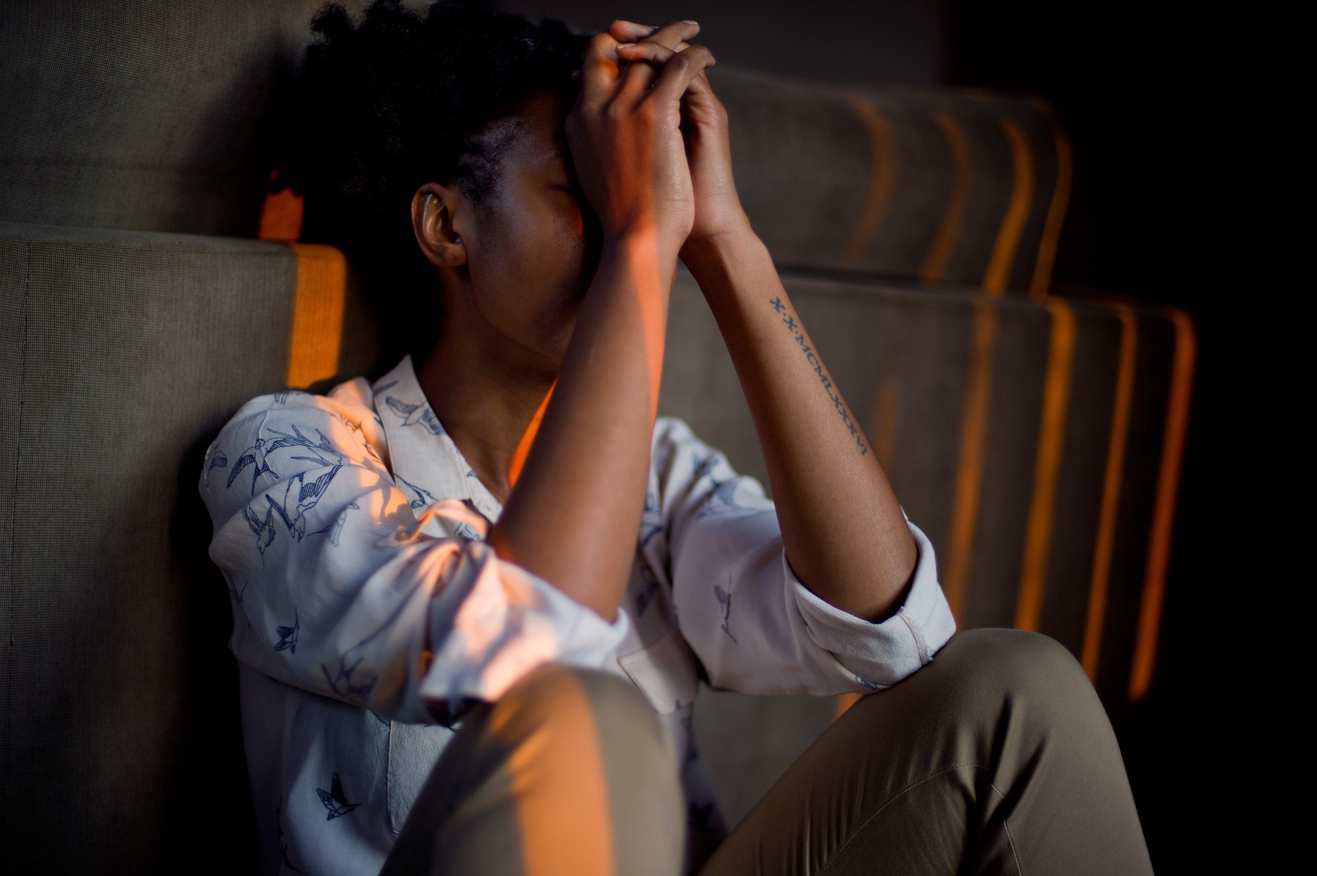A younger Afro-Caribbean woman sitting with her head in her hands looking in pain.