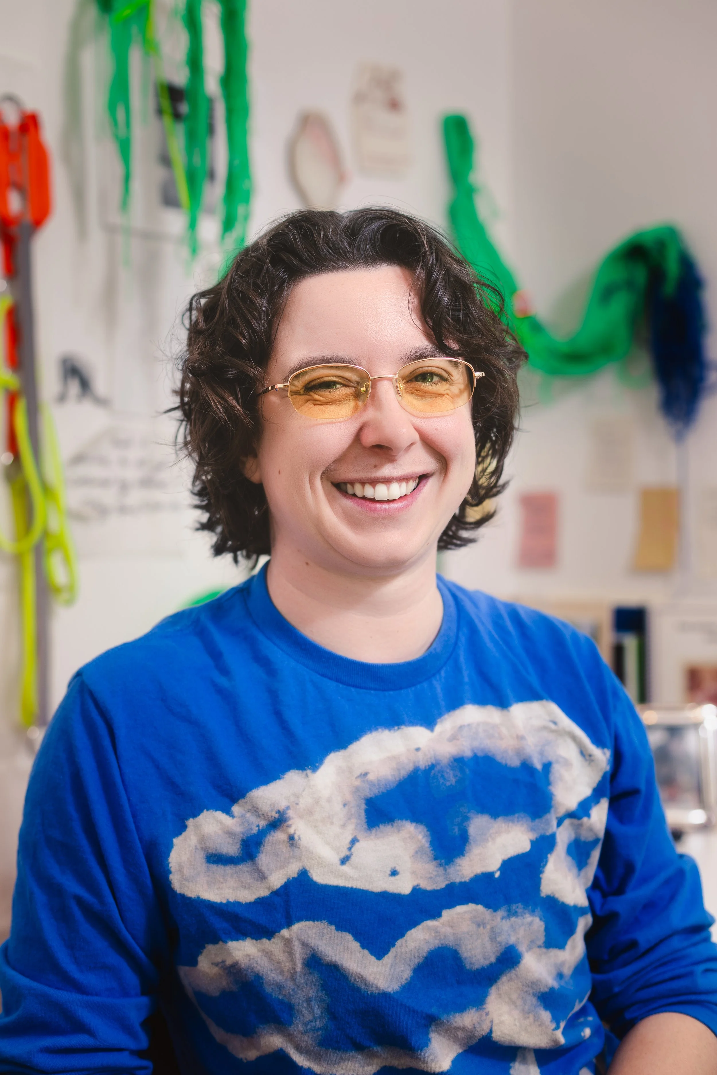 Headshot of an artist wearing orange tinted glasses and a blue t-shirt