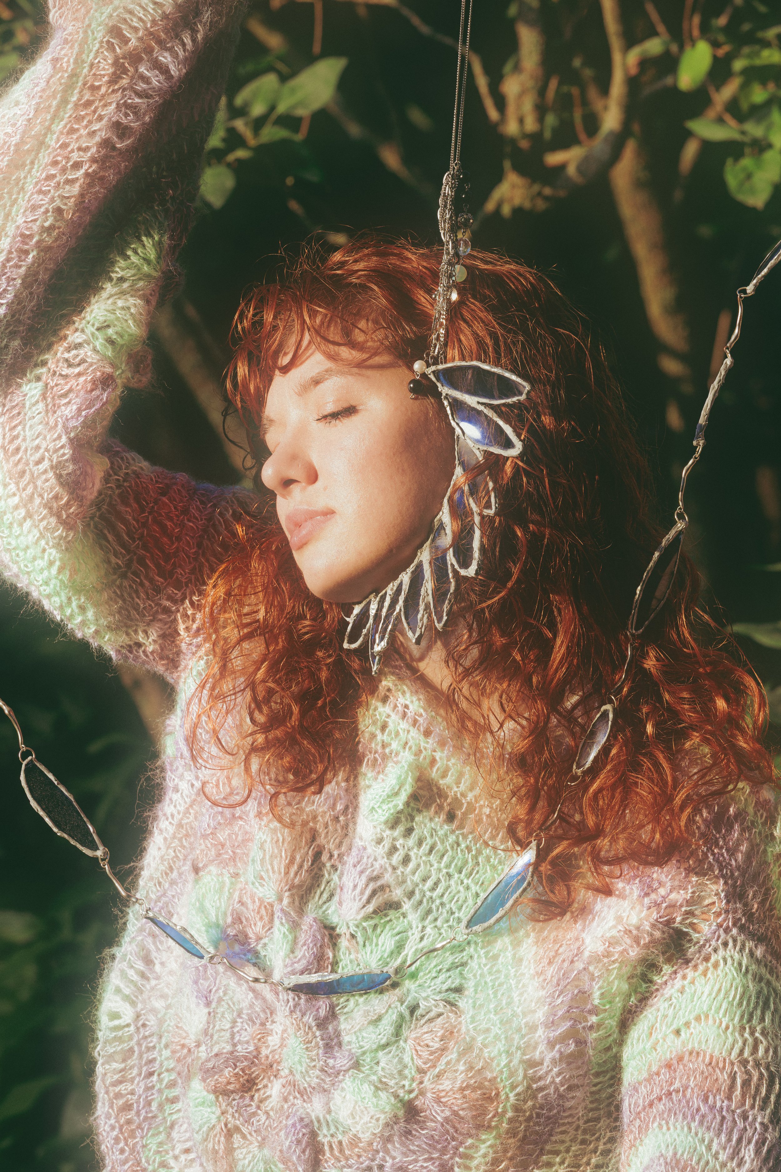 Ethereal portrait of a red haired model wearing a hand knit sweater set against a leaf backdrop