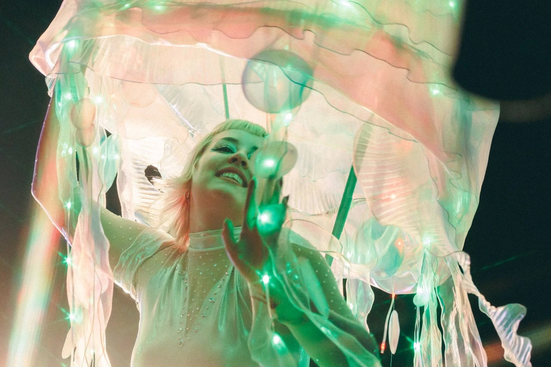 A woman performer dances with a giant jellyfish under green light