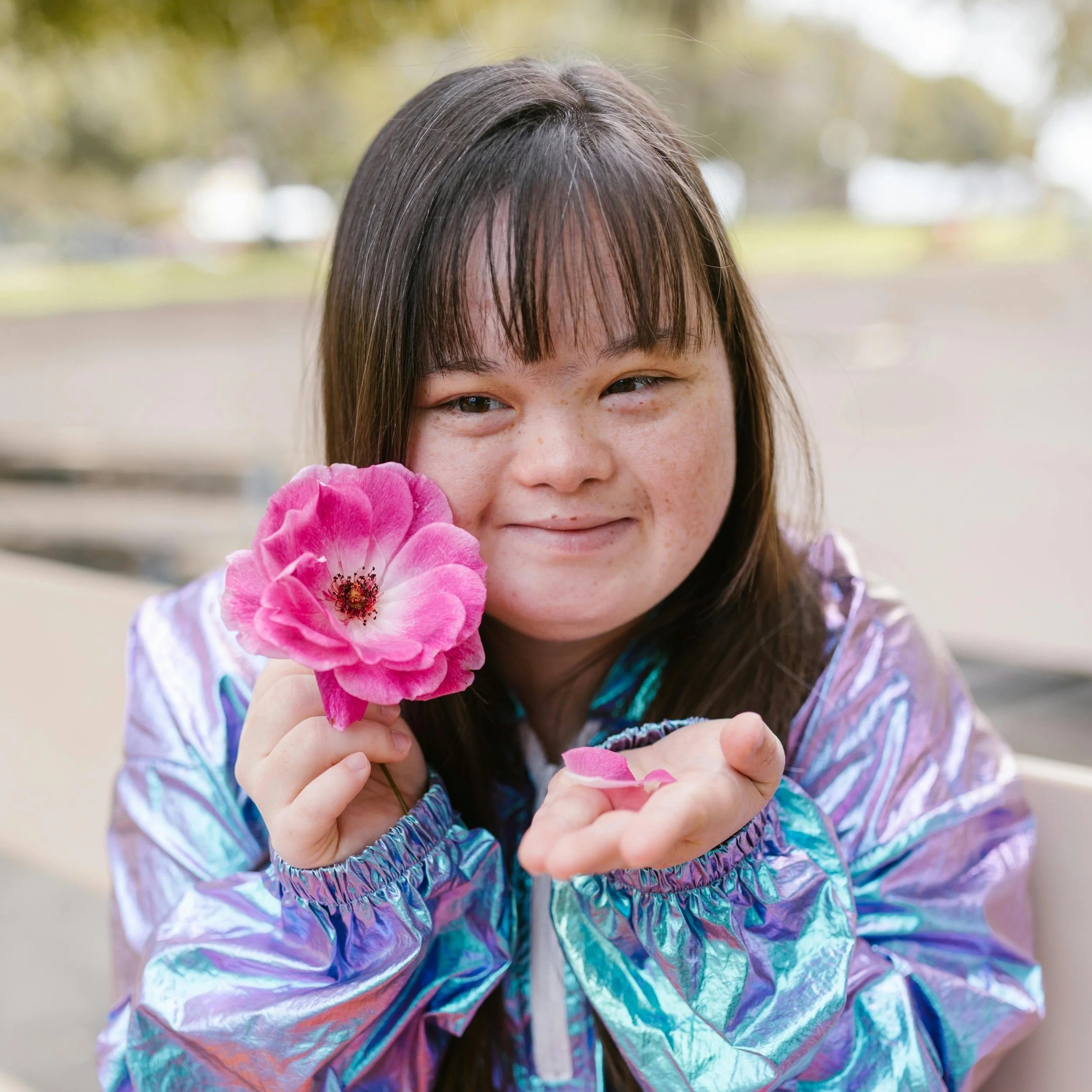 A preteen who lives with Down Syndrome holds a flower and smiles