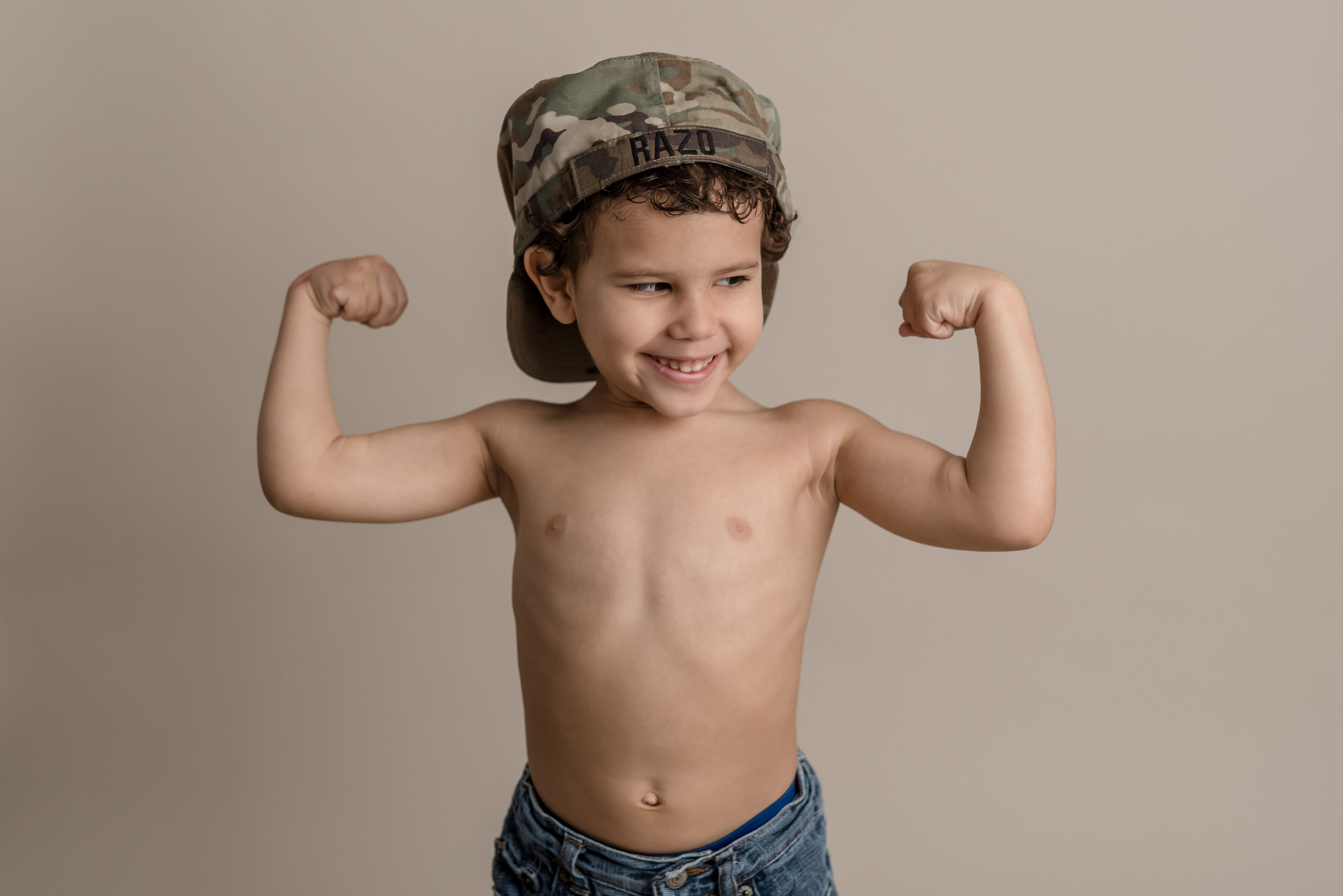 little boy showing off his muscles in his dad’s army hat with junebug photography studio in manhattan, ks