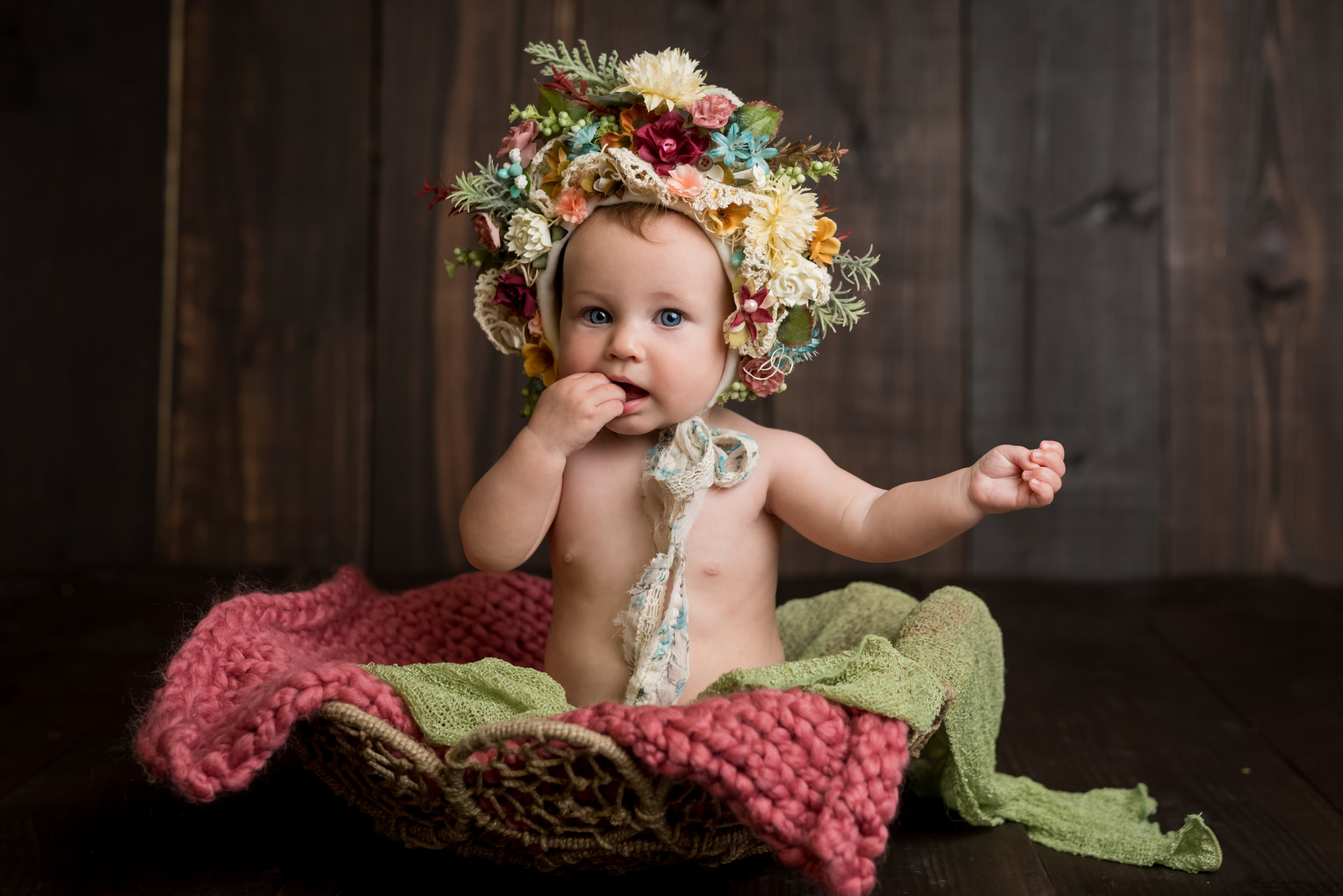 sweet girl sucking on her fingers in a floral bonnet during a sitter session with junebug photography studio in manhattan, ks