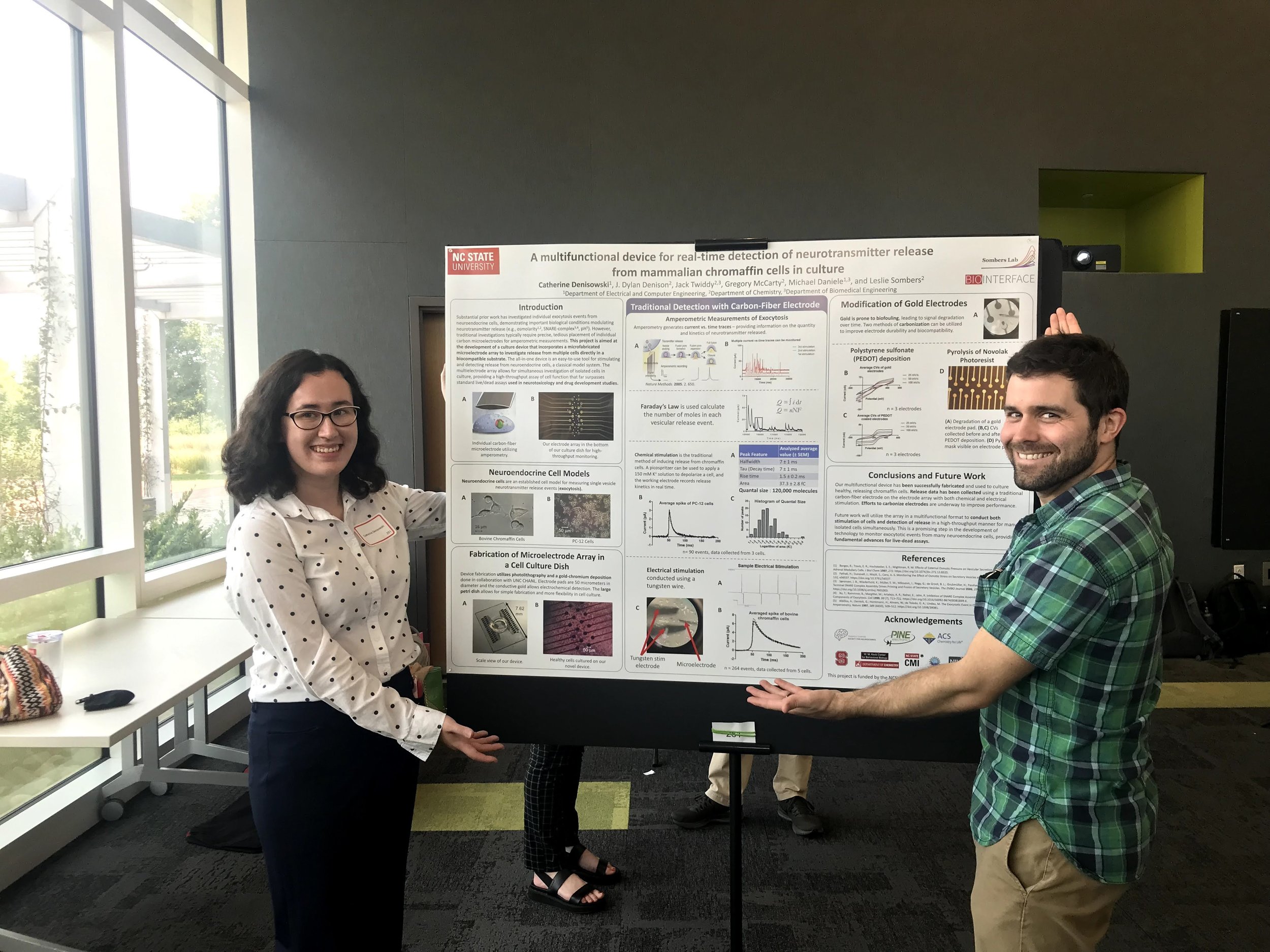  Catherine Denisowski (left) with her research mentor Dylan Denison (right) pose in front of her poster detailing work in creating an electrode-petri dish hybrid 