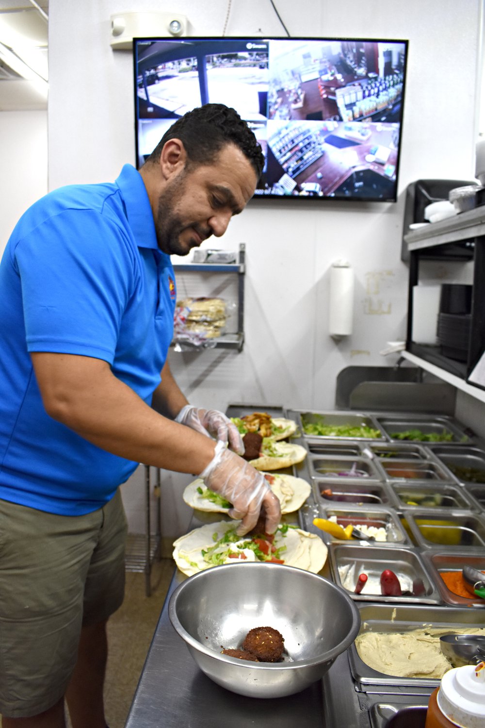  Omar Abouzaid, manager of Al Basha Mediterranean Grill, assembles a sandwich order while keeping an eye on a CCTV of the market next door. When a customer at the market approaches the register, "I sprint over" to complete the transaction, he said. (