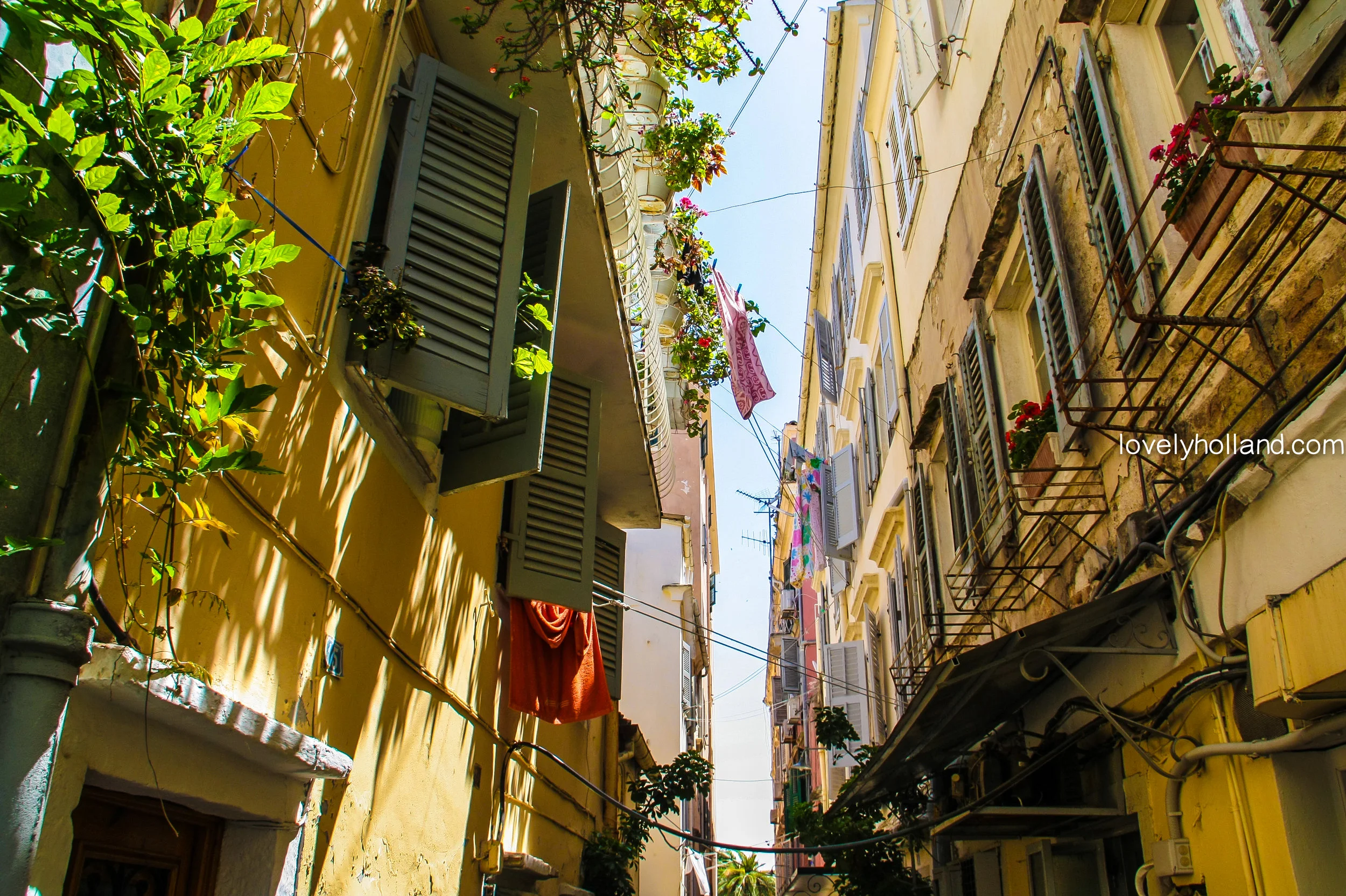 經典南歐街景：可愛百葉窗，黃色外牆，一排排曬著太陽的衣服。