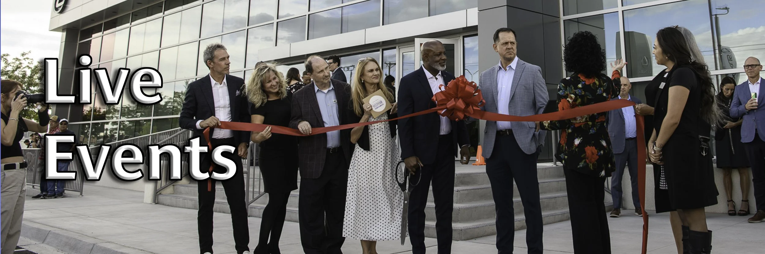 A group of people gathered outside a modern building for a ribbon-cutting ceremony, with some holding scissors and others waiting. A woman with curly black hair is cutting a red ribbon, and a photographer is taking pictures. The words "Live Events" are overlaid on the image.