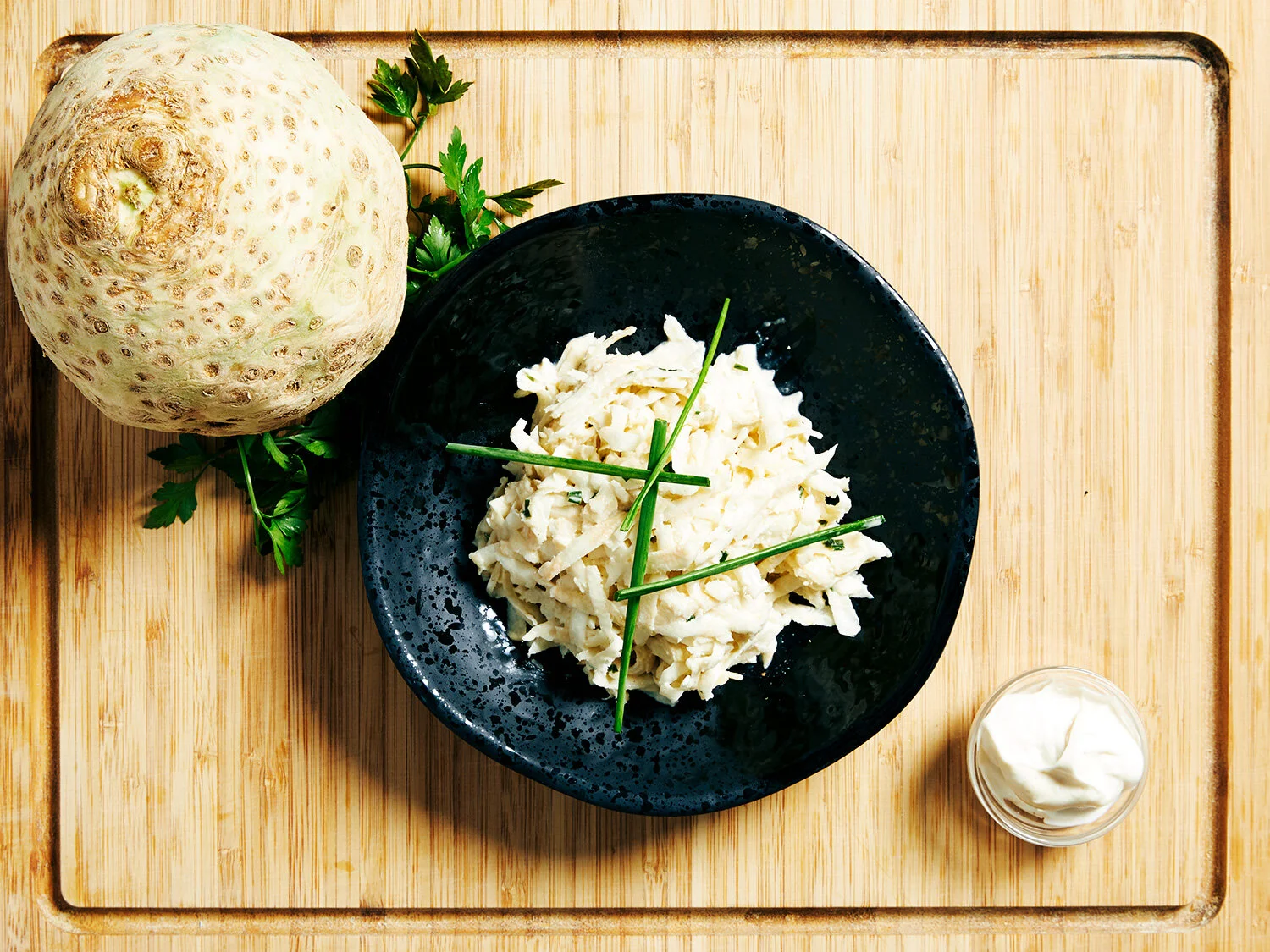 Celeriac Remoulade served on a black plate on a wooden board. Garnished with whole celeriac and garlic