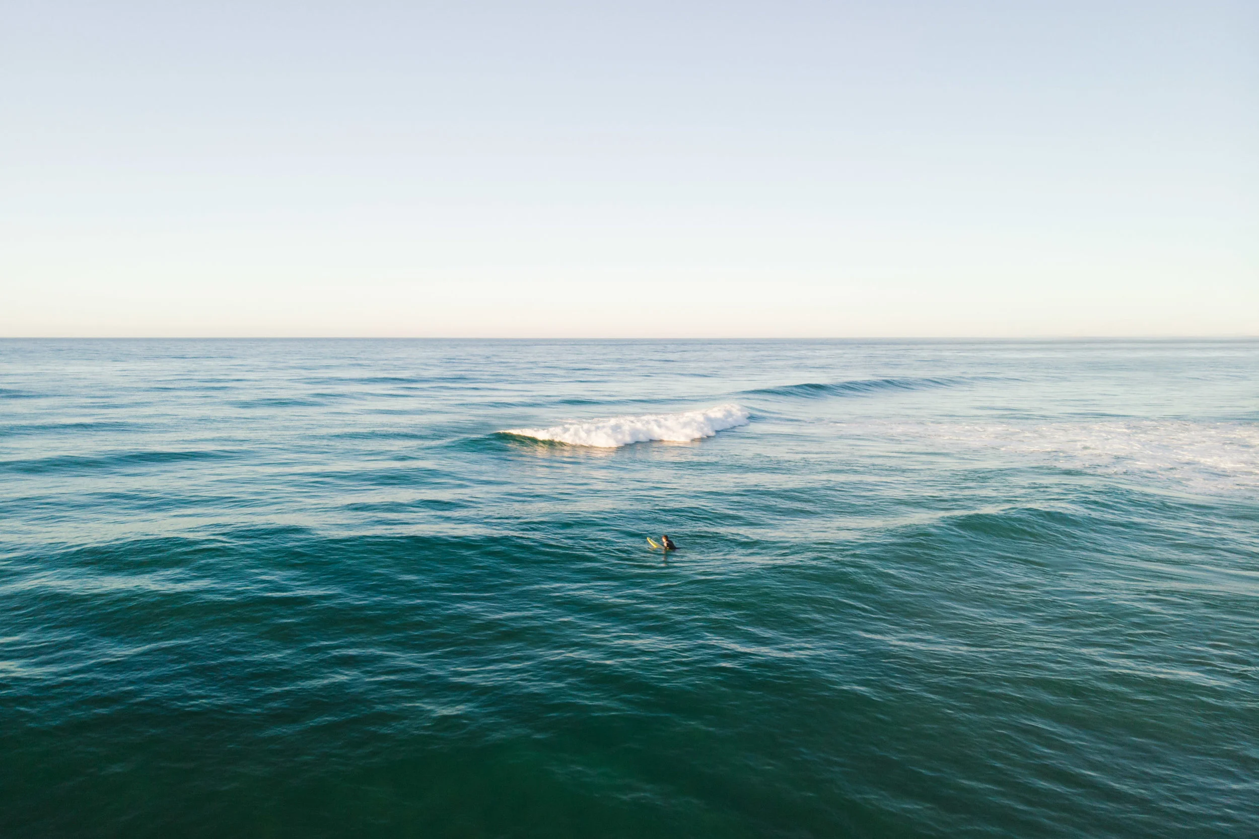 Blue ocean with surfer and wave breaking at sunset.
