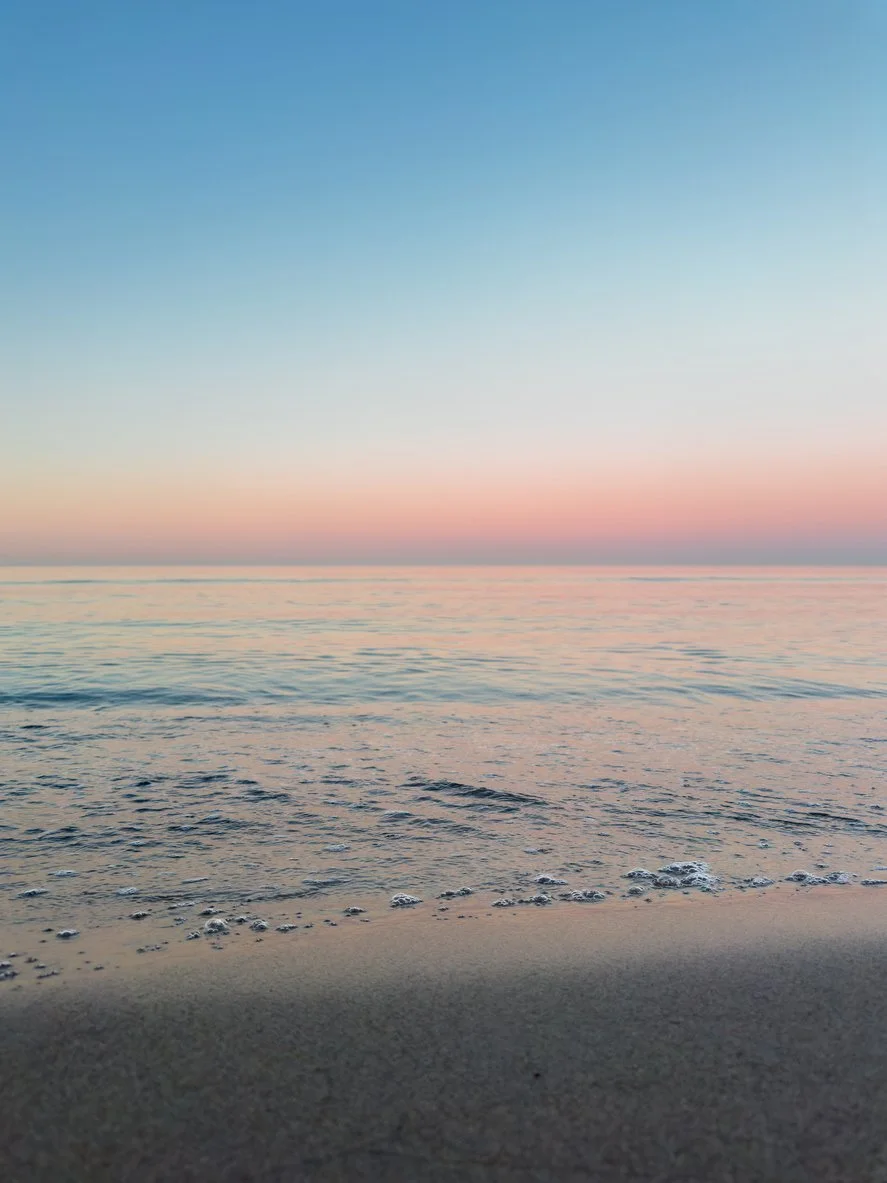 Soft ocean waves meeting a pastel pink and blue sunset horizon, creating a peaceful sense of space, calm, and renewal.