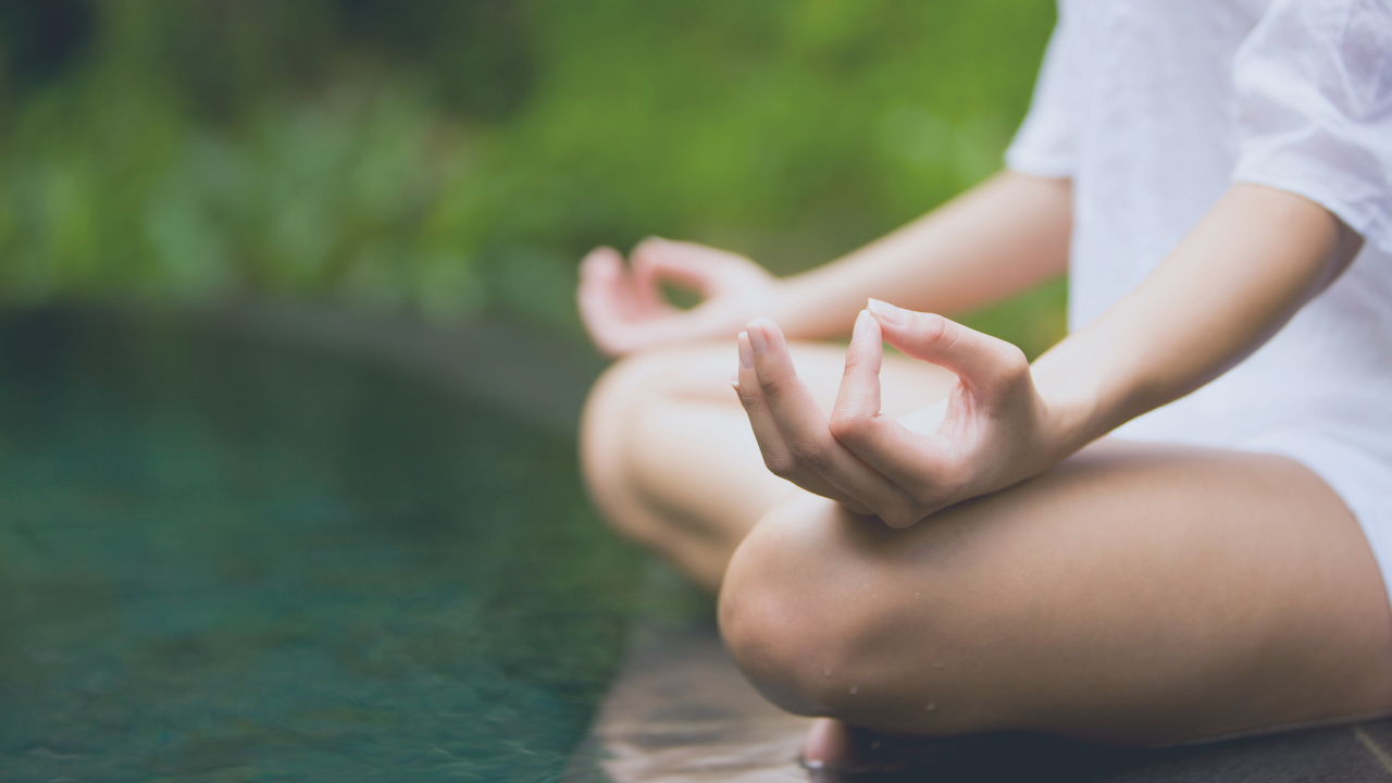 Person seated in meditation beside calm water, representing guided breathwork and nervous system regulation through the Breathe With Me program."