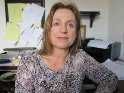A woman sits at a desk surrounded by papers. 