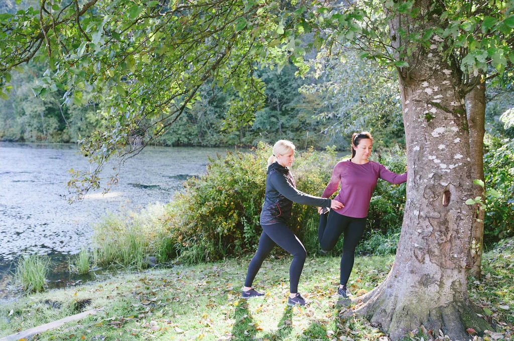 Personal trainer guiding clients through outdoor stretching exercises by the river in Pemberton, BC.