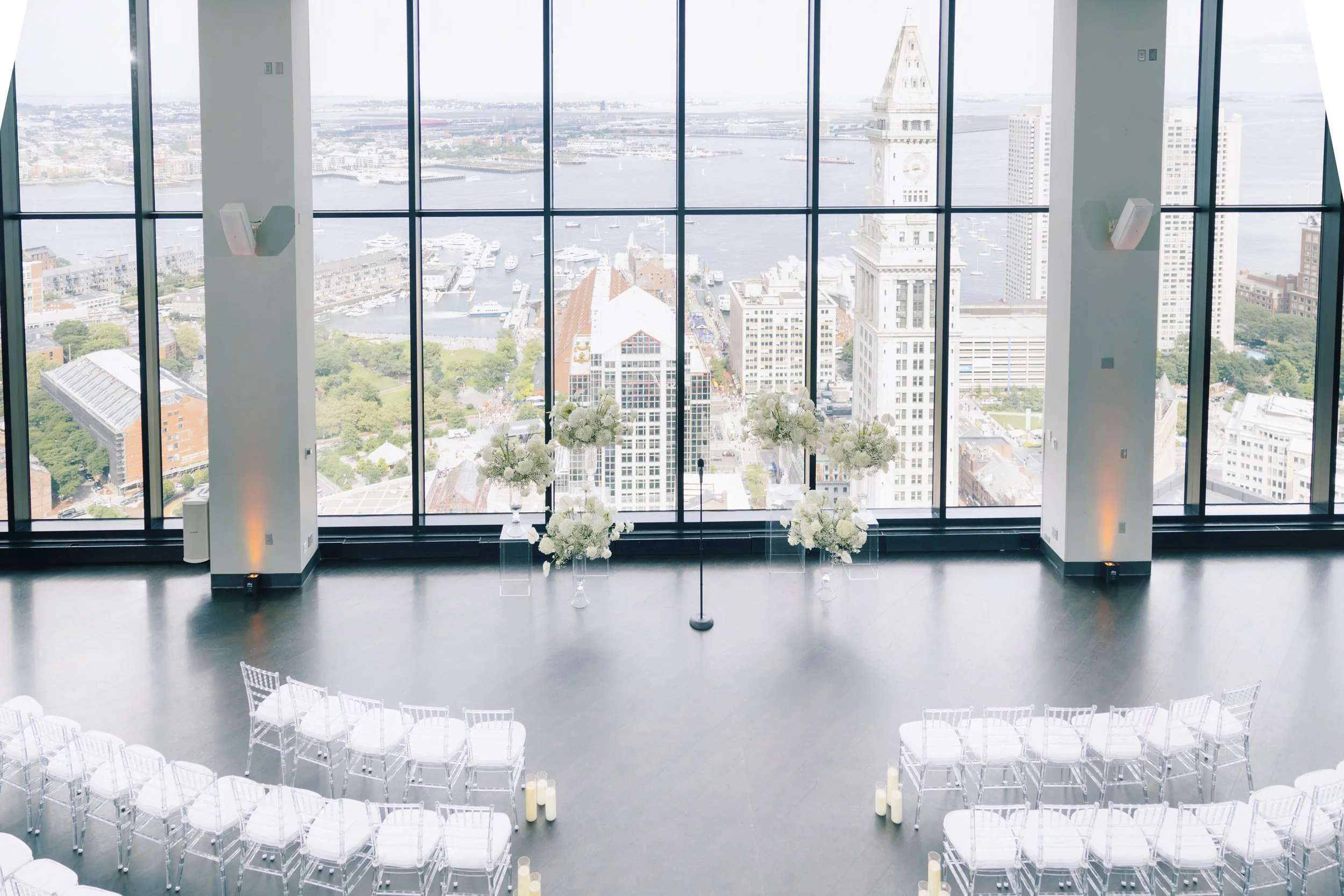 Clear acrylic chairs with white cushions in semi-circles overlook floor to ceiling windows with white floral archway