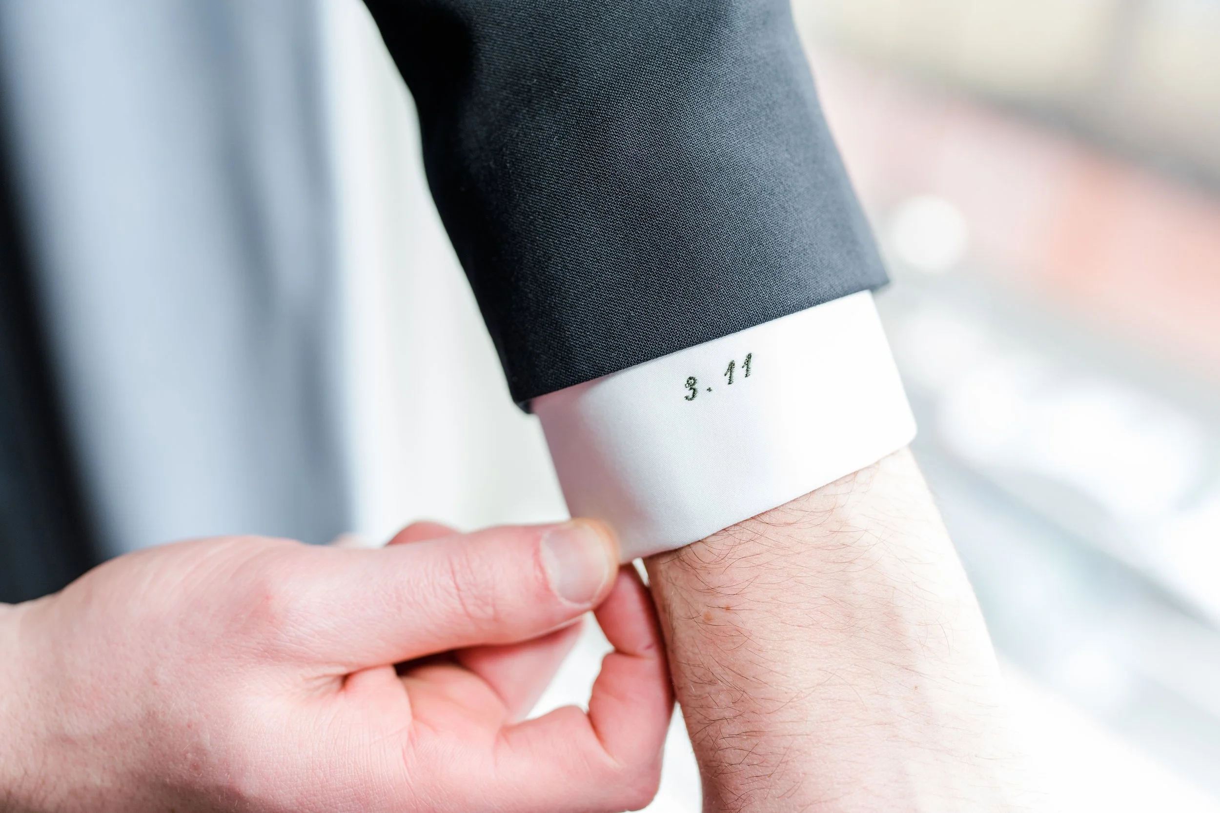 A black suit sleeve showing off a white mens button up with a wedding date embroidered on the white sleeve.