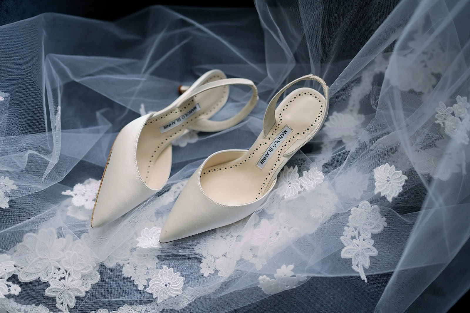 Two white high heels on a white veil with foral lace detailing