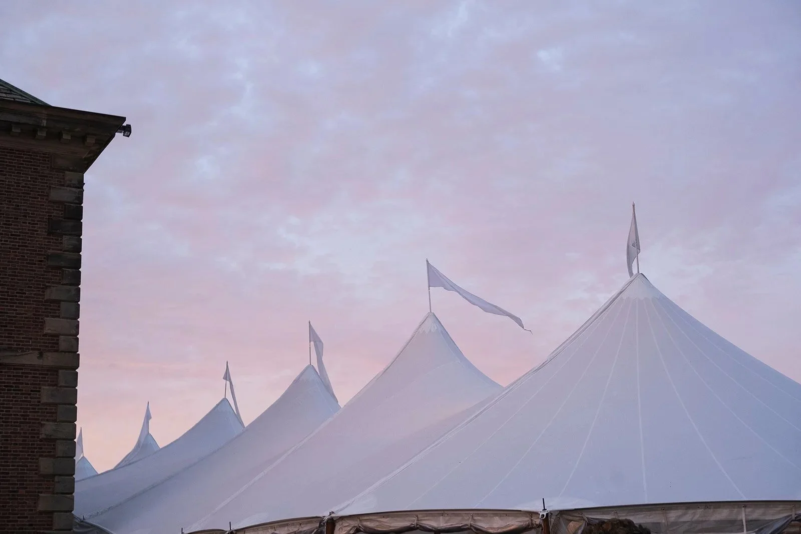 White sailcloth tent with five peaks with a soft purple sunset