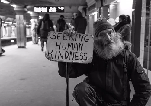 A man holding a sign asking for human kindness