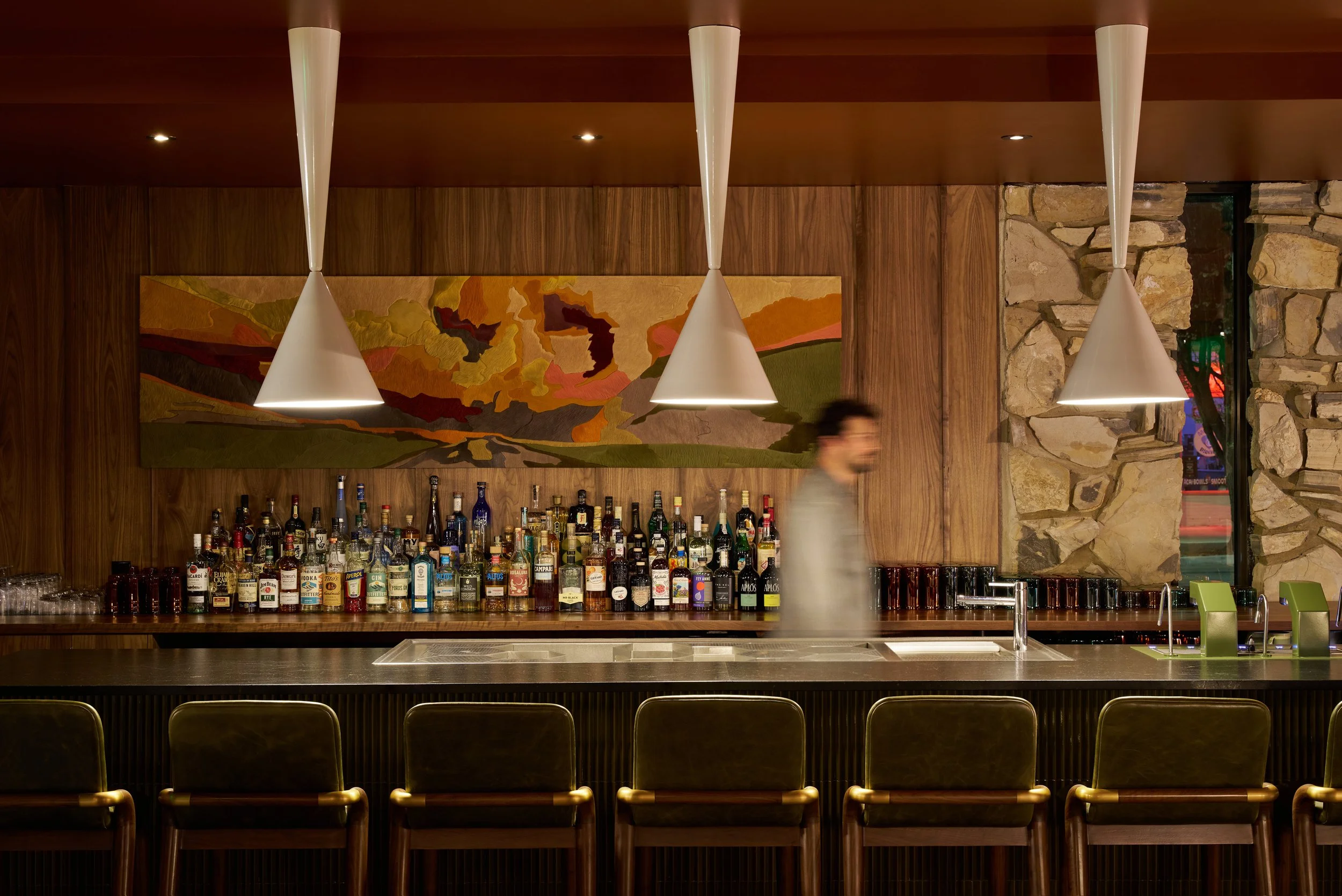 All Is Well lobby bar at the All Inn Hotel in Denver, Colorado, designed by Maximalist, featuring walnut paneling, natural stone, sculptural lighting, and mid-century modern interiors.