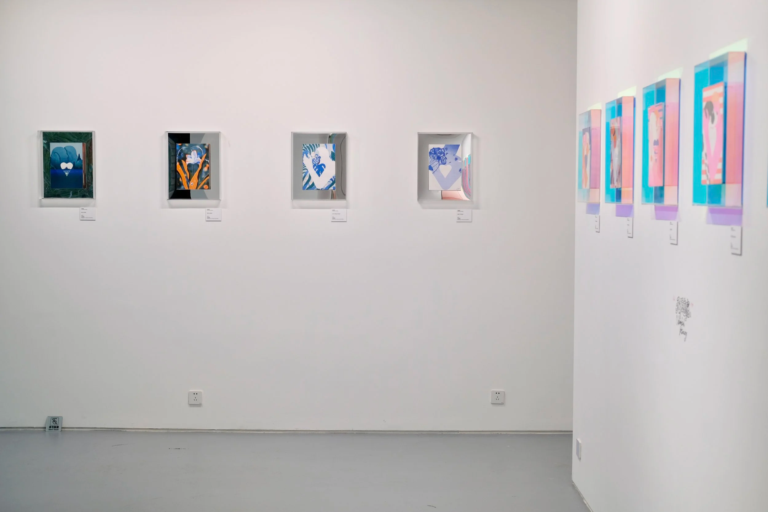 Art gallery wall displaying six colorful abstract paintings in white frames, with additional artworks reflected on the right wall.