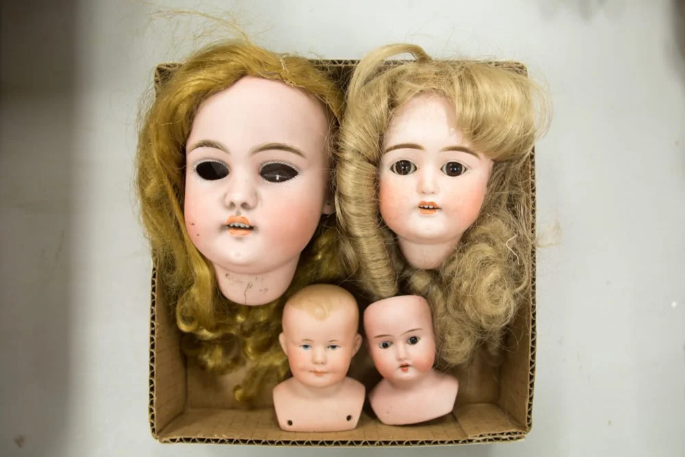 A box lot of doll heads sits on a table waiting to be sorted and sold at a future auction .