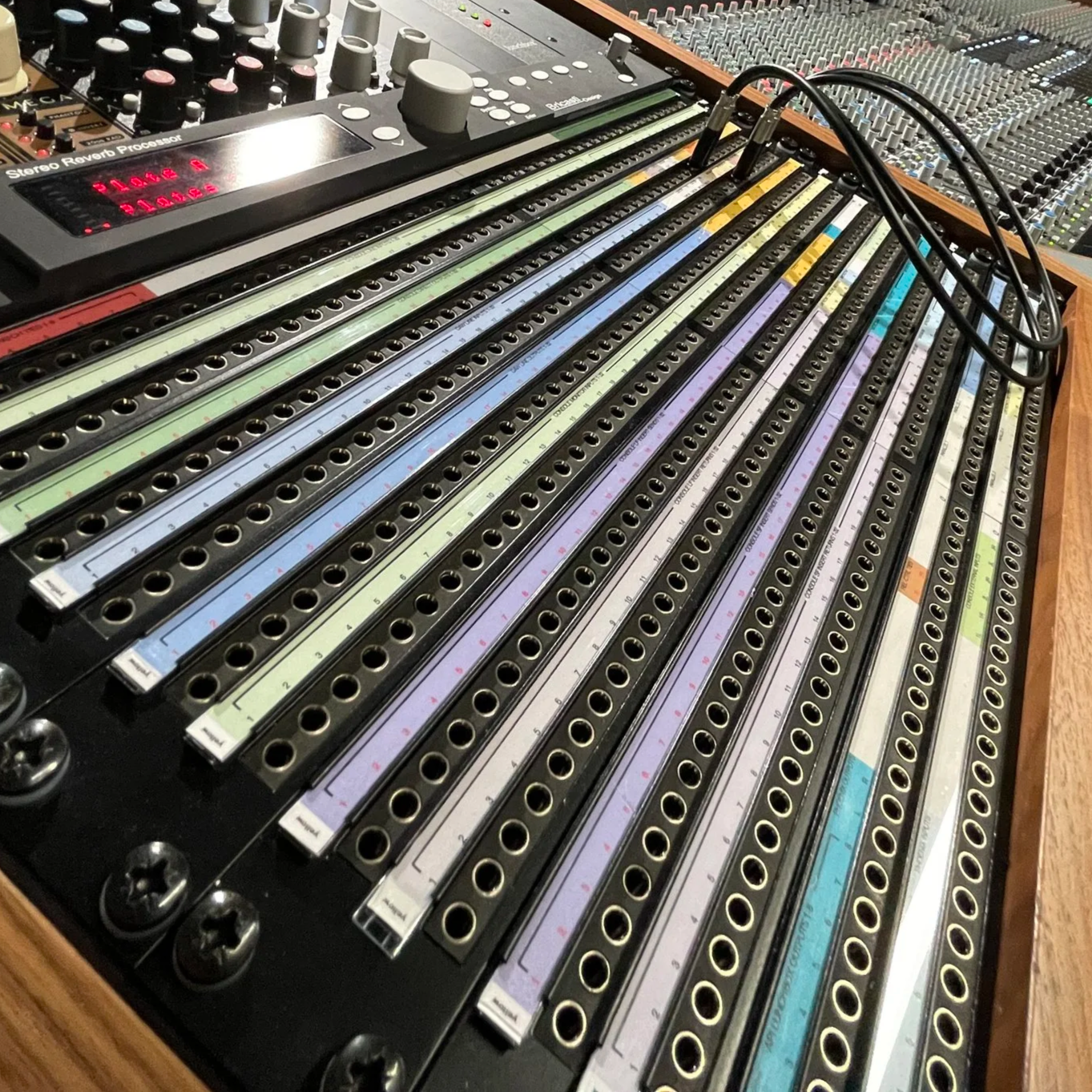 A patchbay with patch cables plugged in and a mixing desk in the background