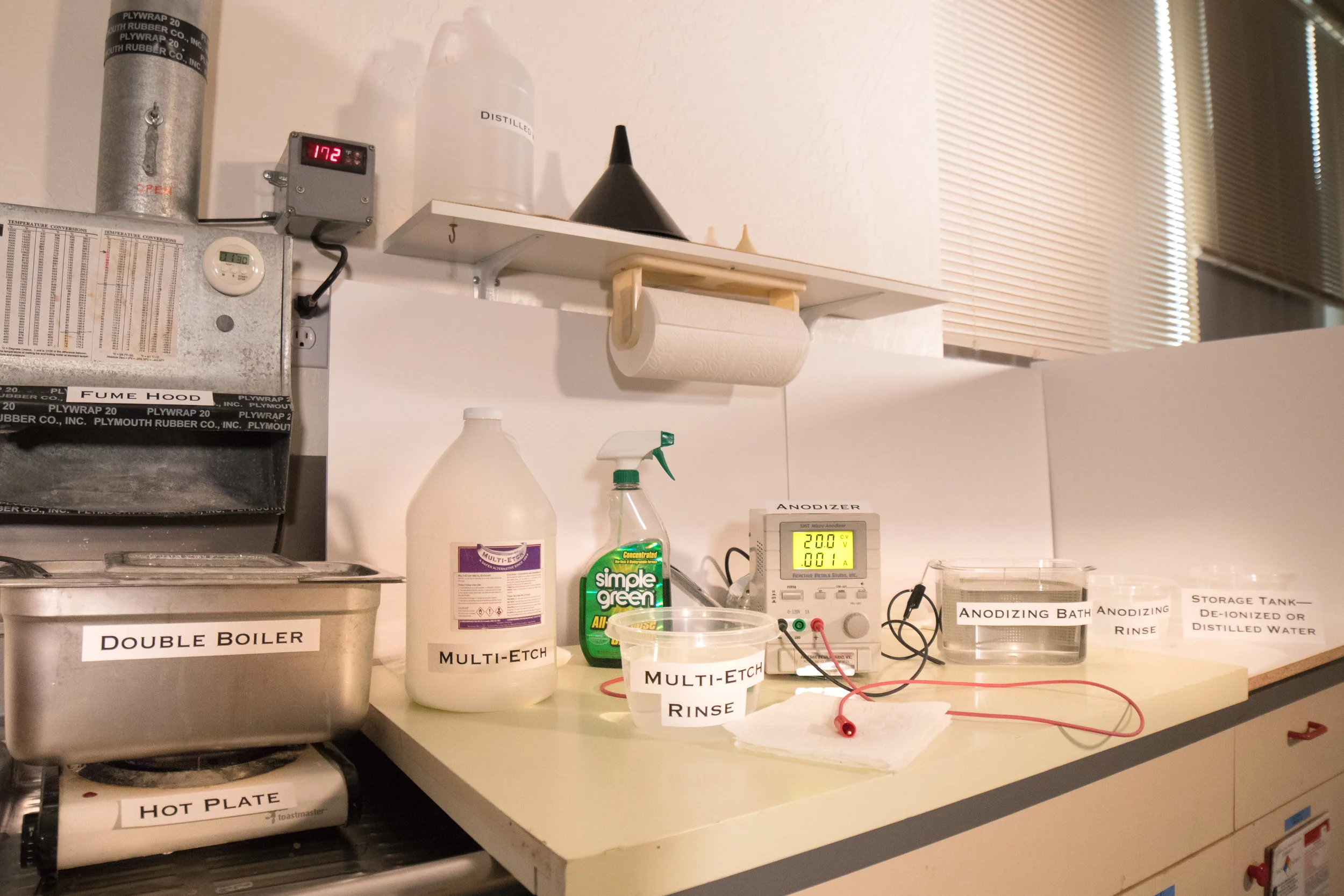 Small laboratory set-up featuring a fume hood above a double boiler. Table next to the double boiler has suggested set-up for anodizing and using multi-etch.