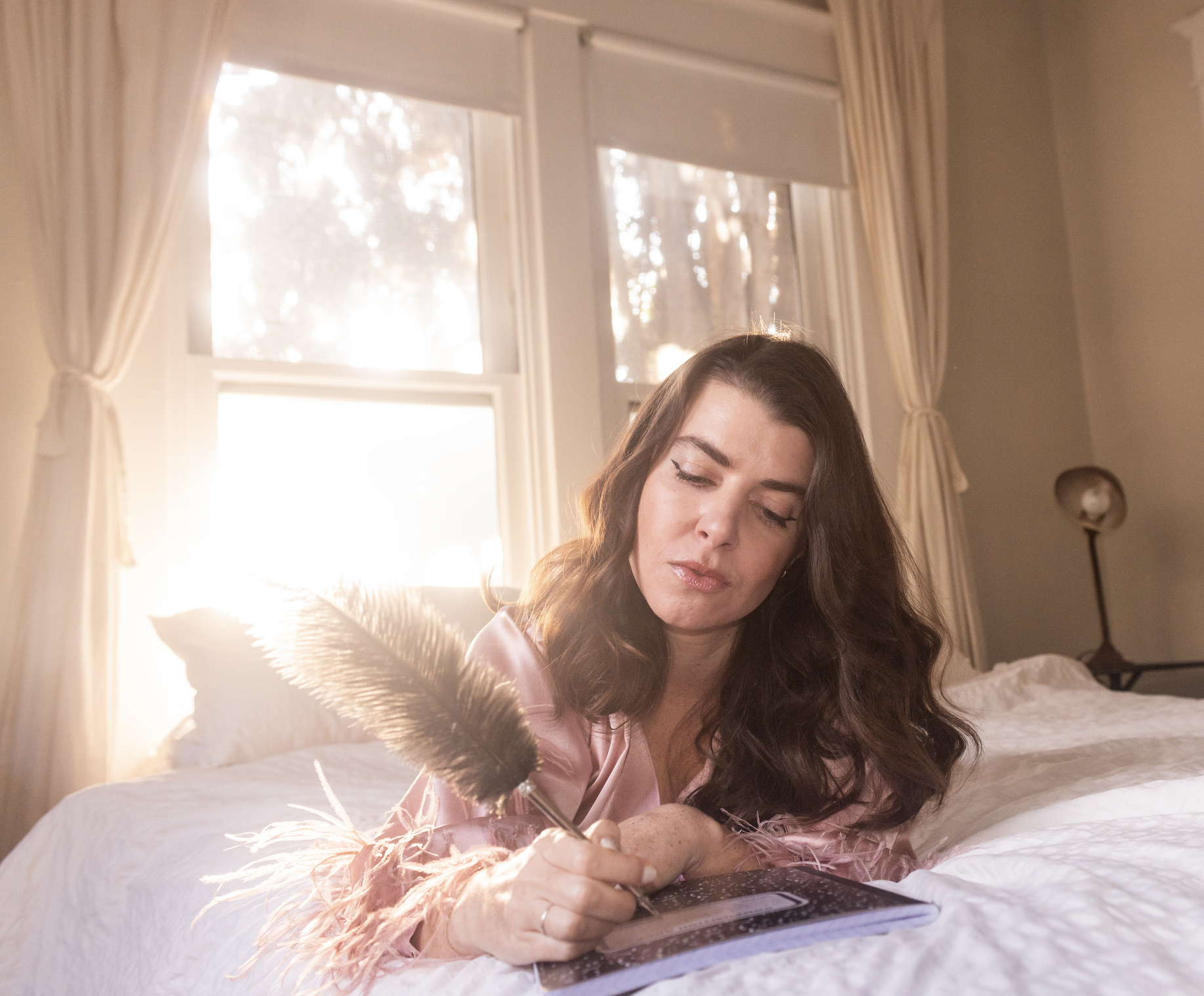 Carly Pifer writes while lounging on bed with a big feather pen
