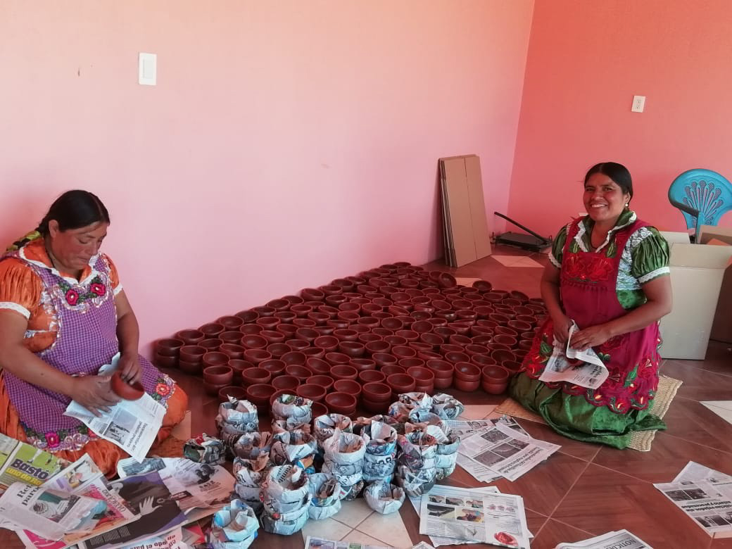 Two artisans wrapping red clay pottery in newspaper.