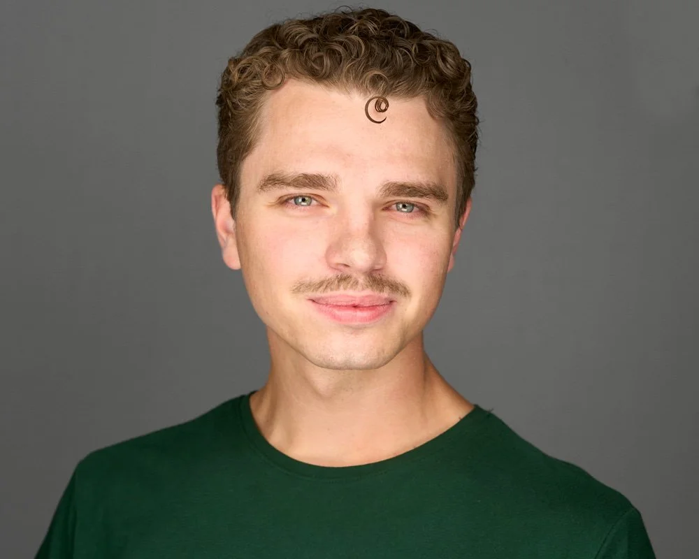 Actor headshot of a male in a green crew neck shirt against a gray background