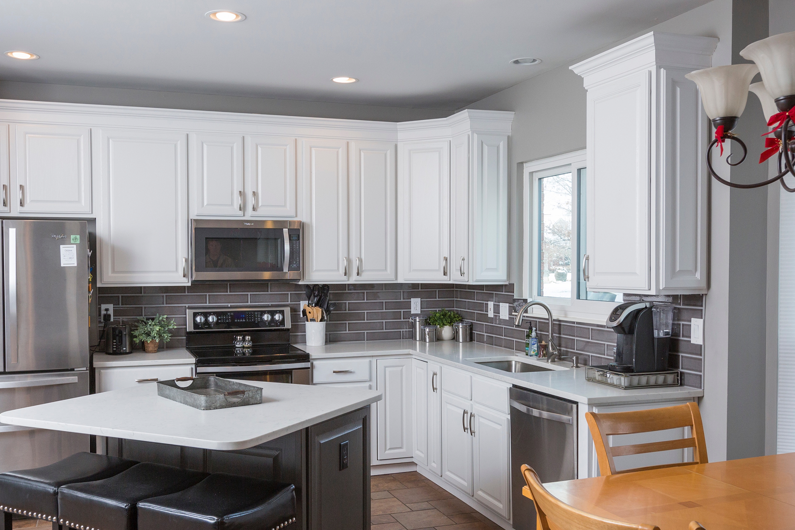 Modern kitchen after a kitchen facelift featuring white cabinets, stainless steel appliances, gray backsplash, and a center island with seating.