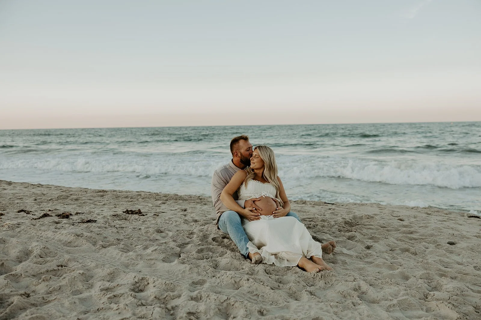 A couple posing for maternity photos sitting on the beach