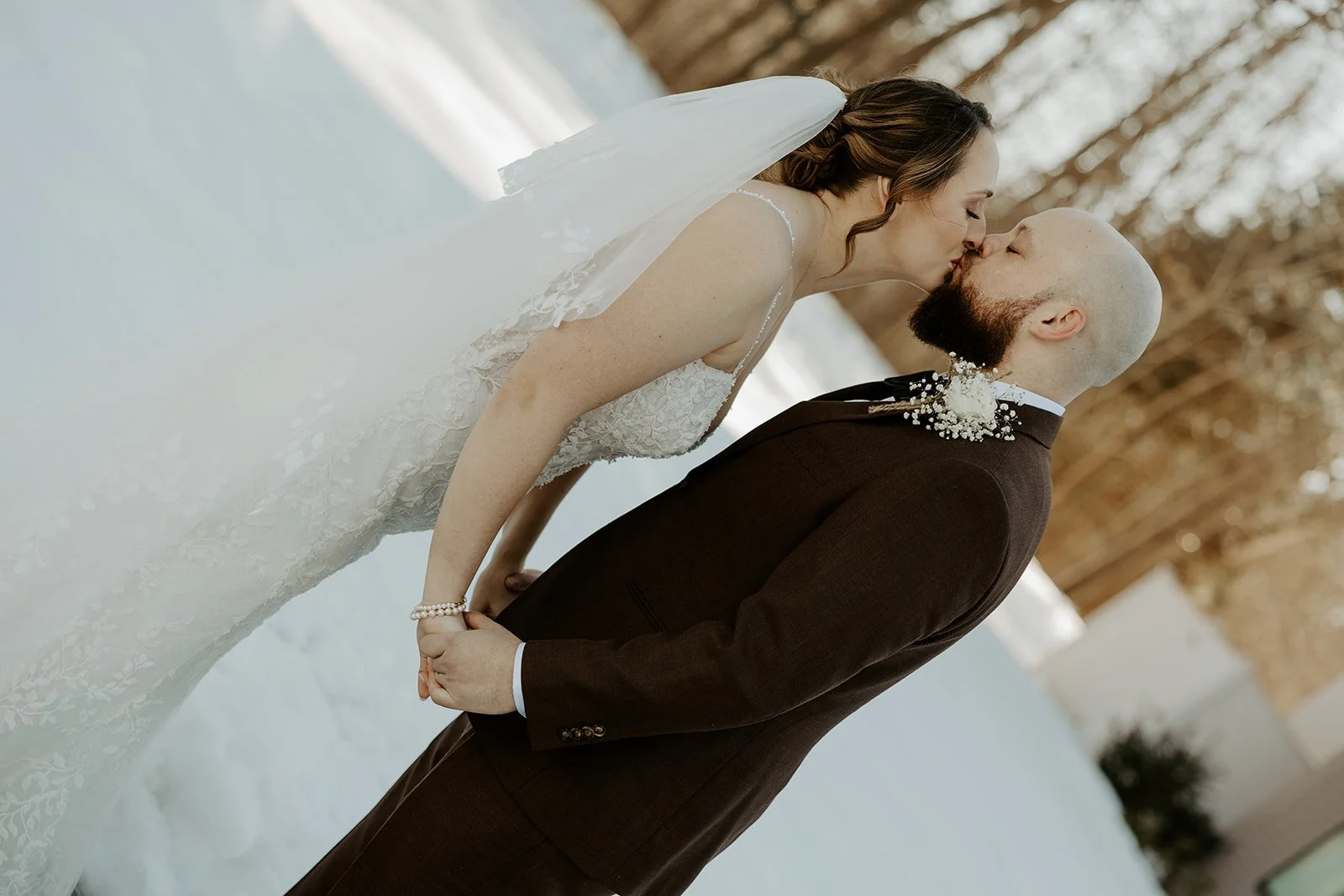 A bride and groom kissing in front of a snowy field