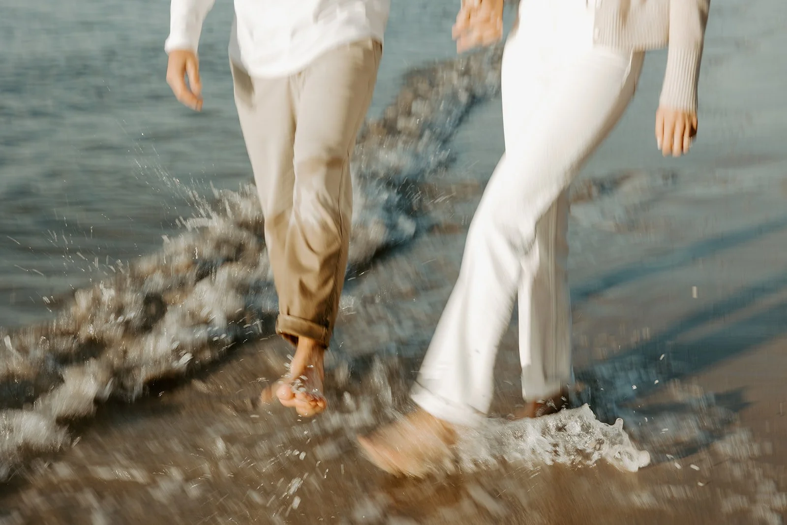 A couple walking through the ocean during beach engagement photos at their Massachusetts engagement photo location