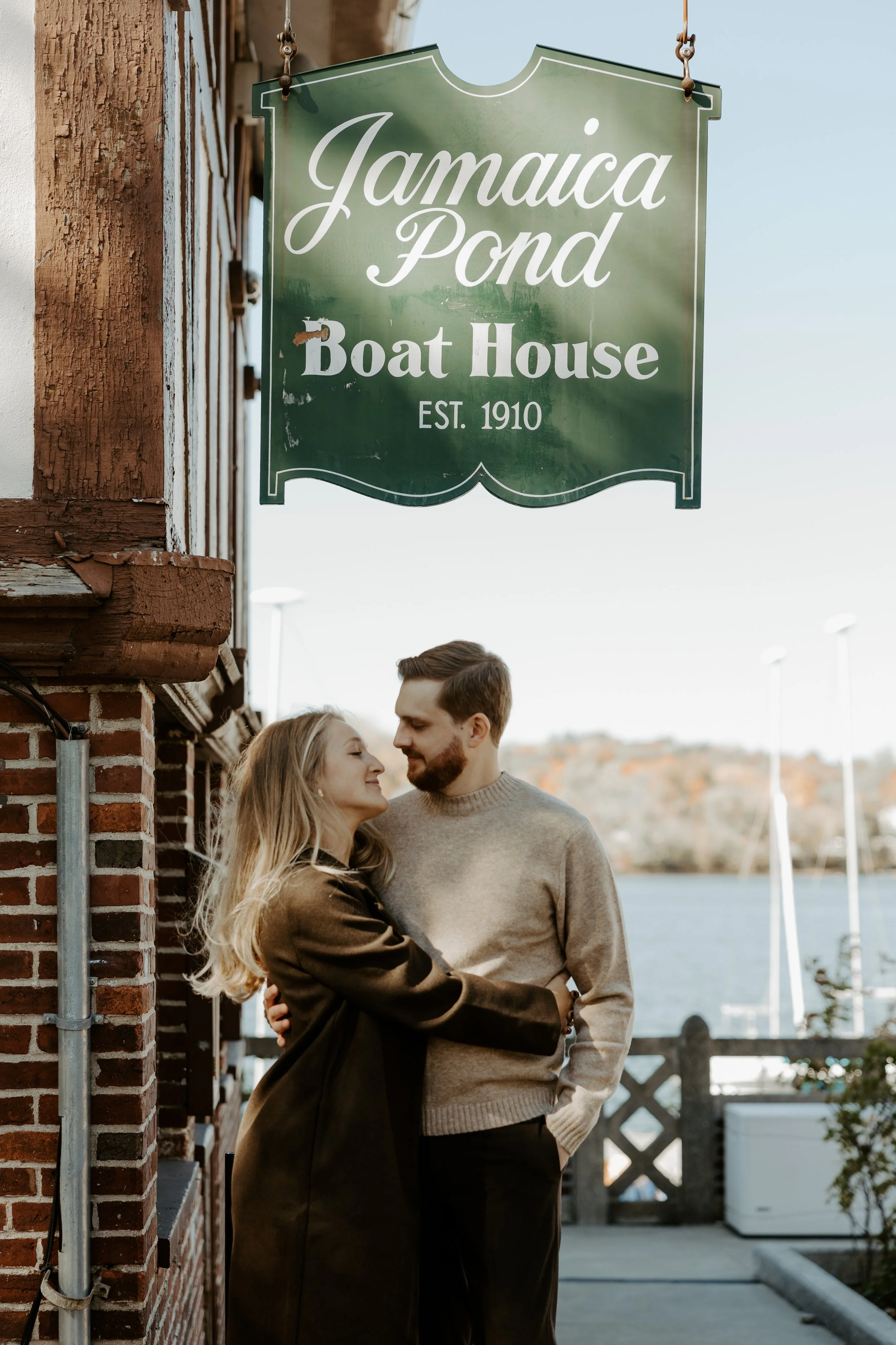 A couple posing for their engagement photoshoot under a sign at Jamaica Pons, captured by a Boston engagement photographer