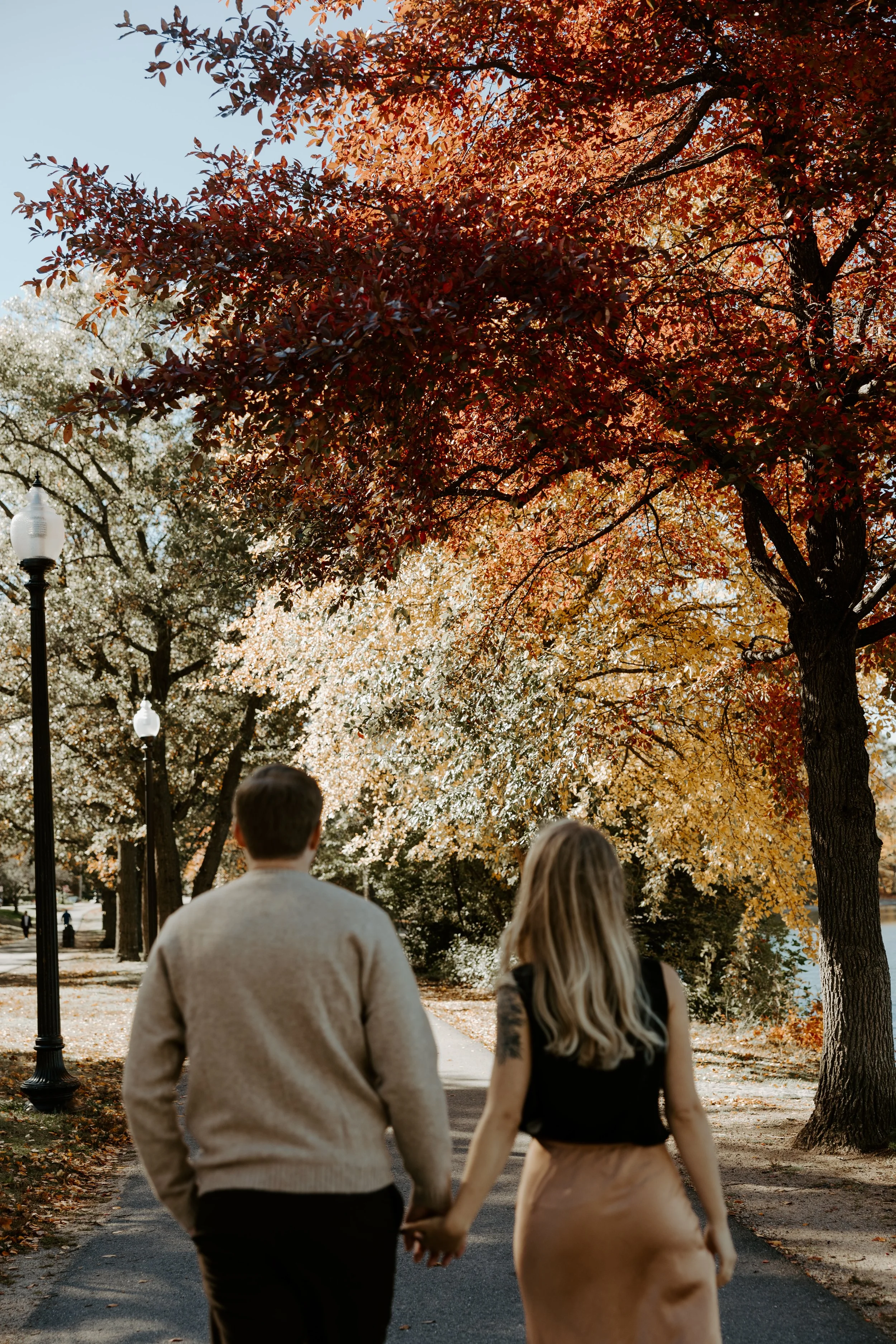 A couple walking along the streets at Jamaica Pond with fall-colored trees above them
