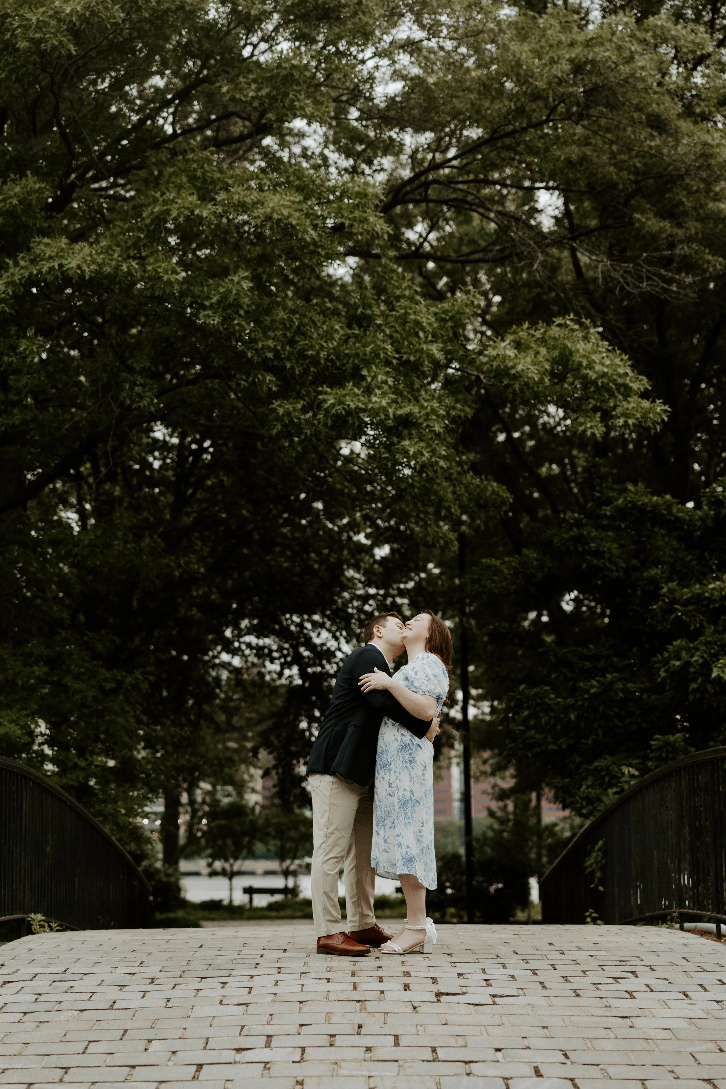 A man kissing his fiancee on a bridge, posed by a Boston engagement photographer