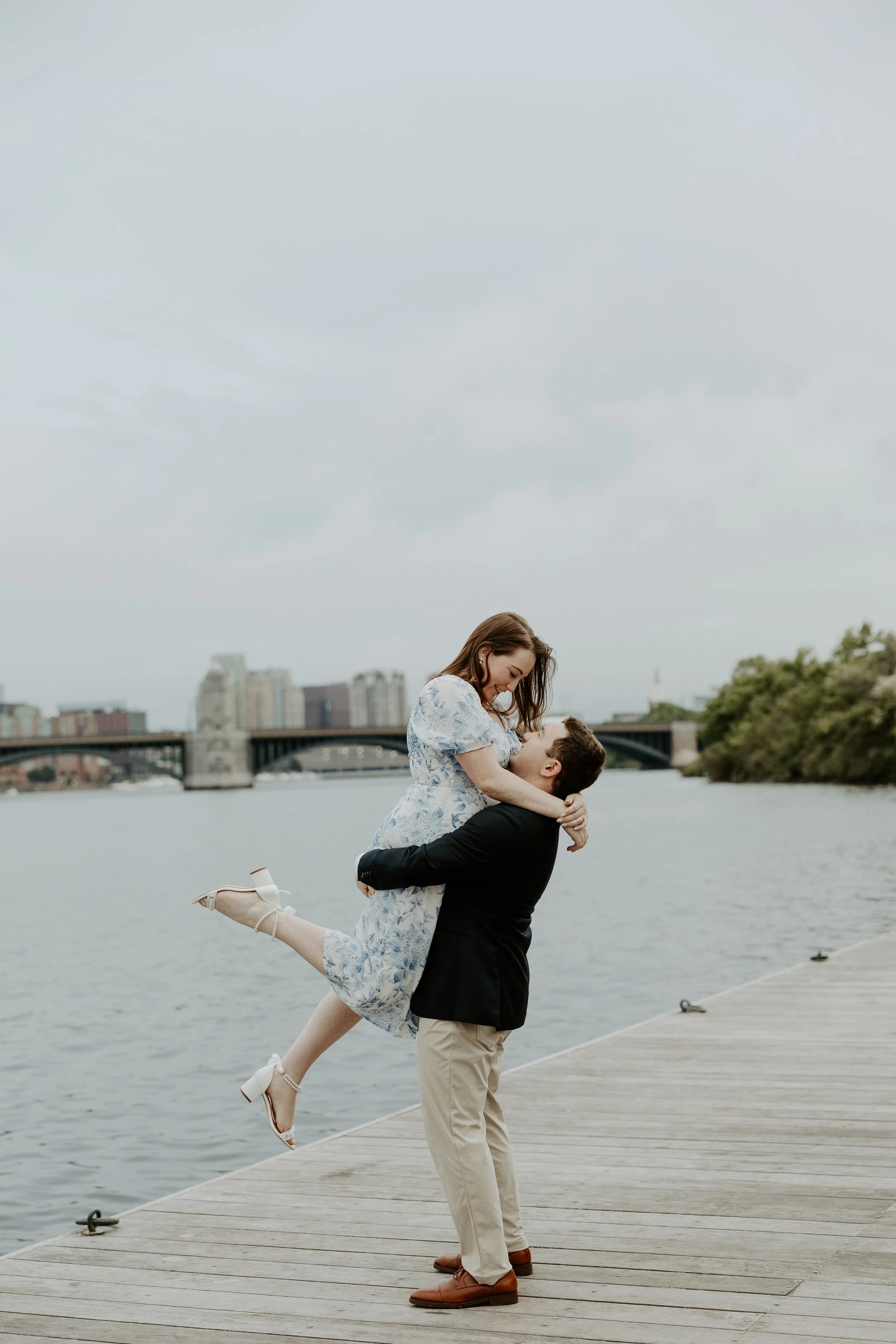 A man lifting up his fiancee on a dock, posed by a Boston engagement photographer