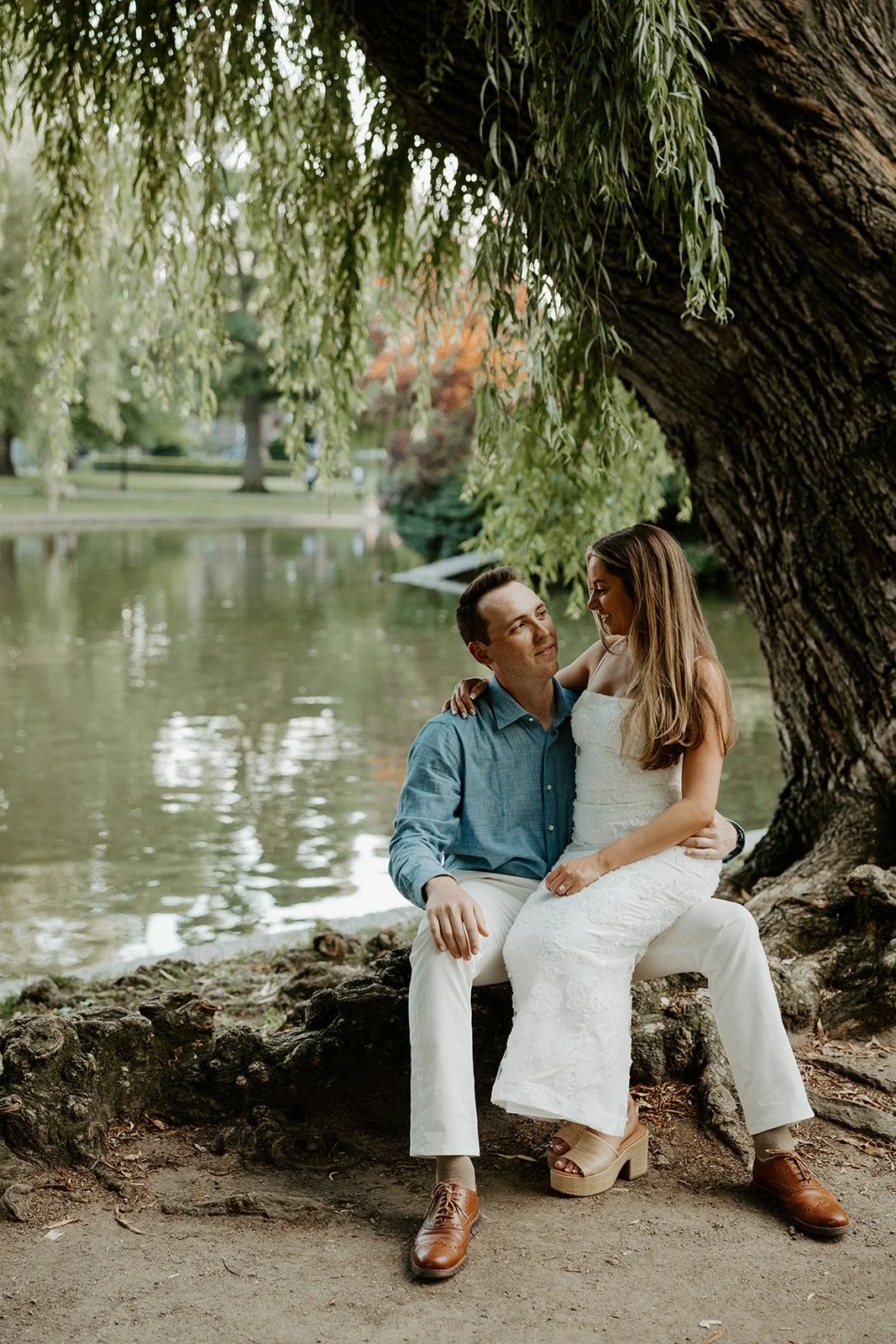A woman sitting on her fiance's lap during engagement photos at Public Garden