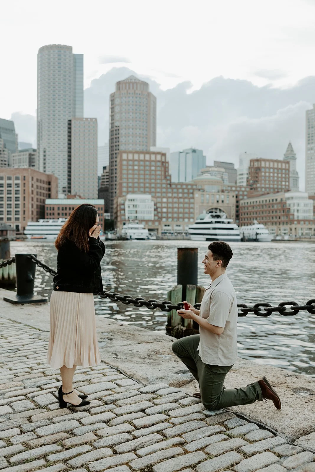 A photo taken by a Boston engagement photographer of a surprise proposal at Fan Pier Park