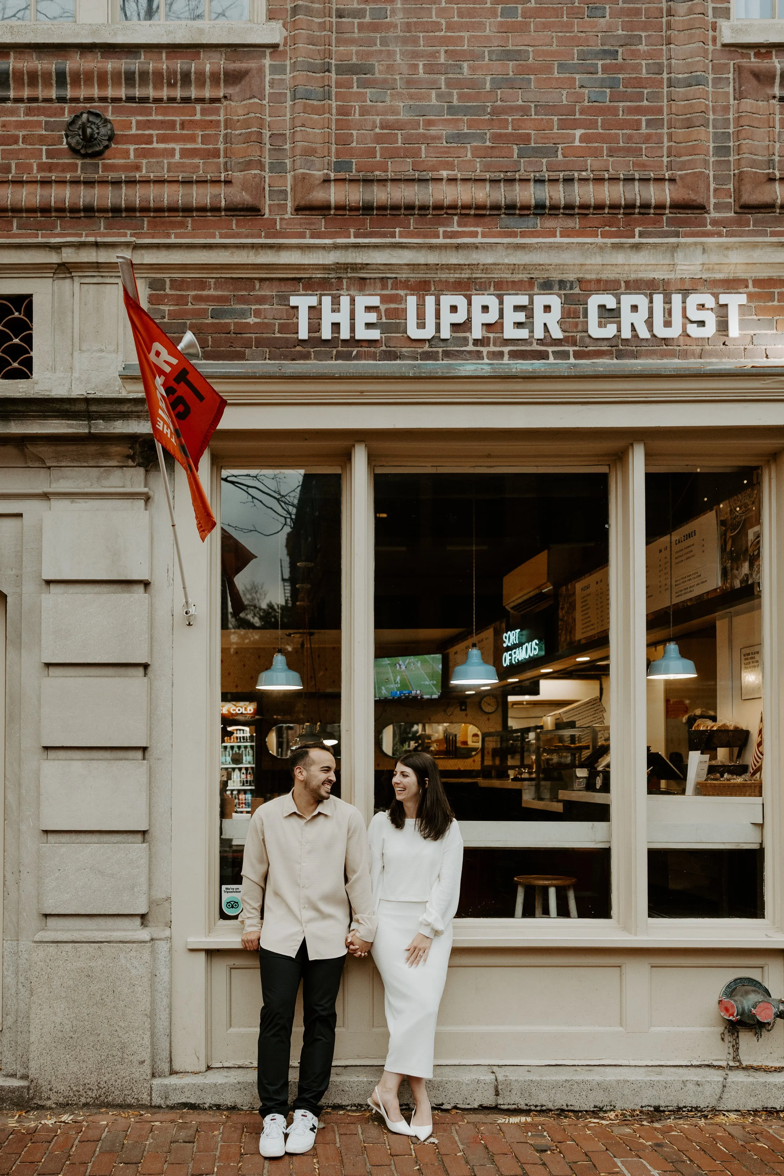 A couple posing in front f a pizza restaurant, captured by a Boston engagement photographer
